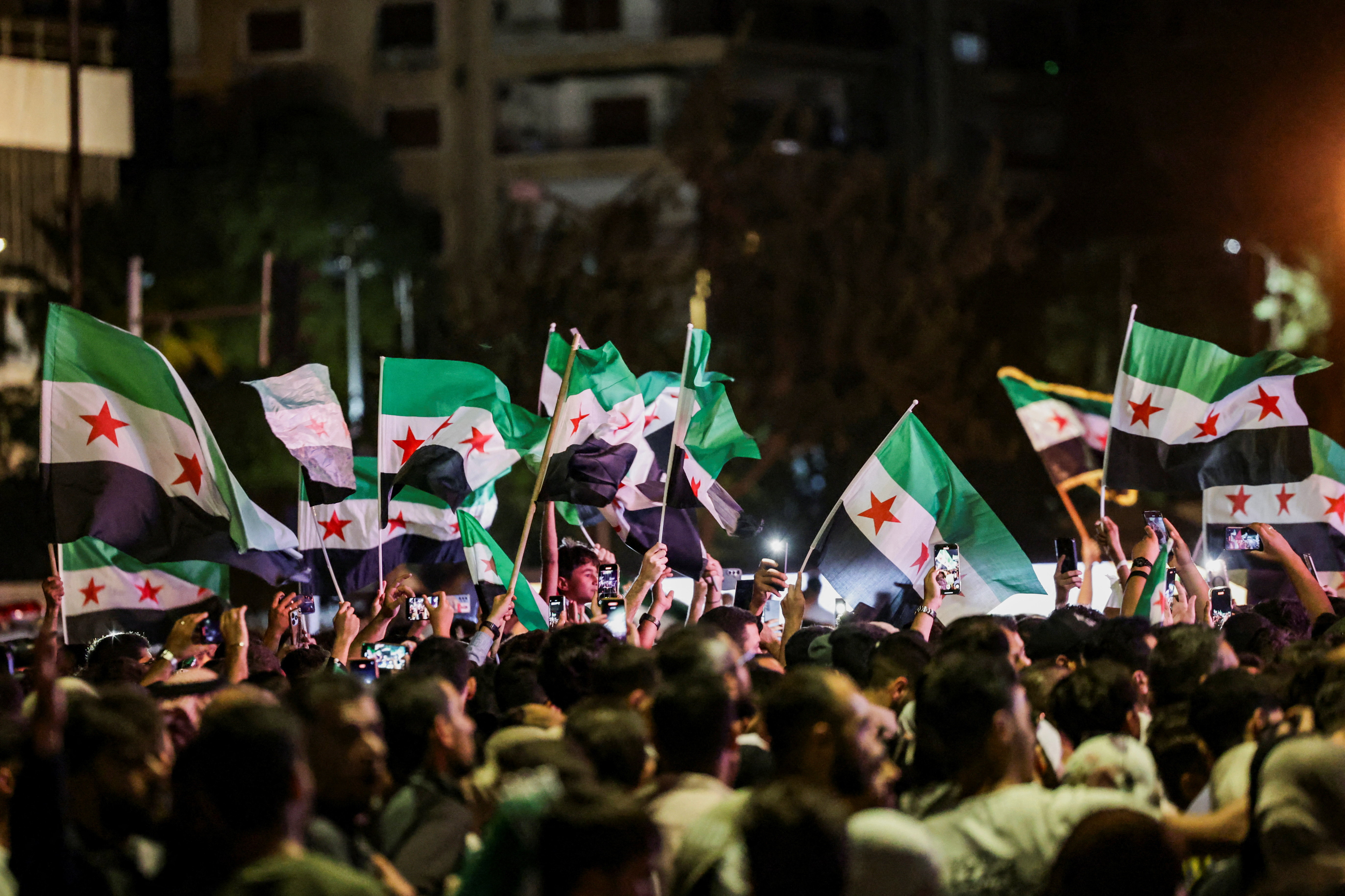 A crowd waves Syrian flags at a nighttime gathering