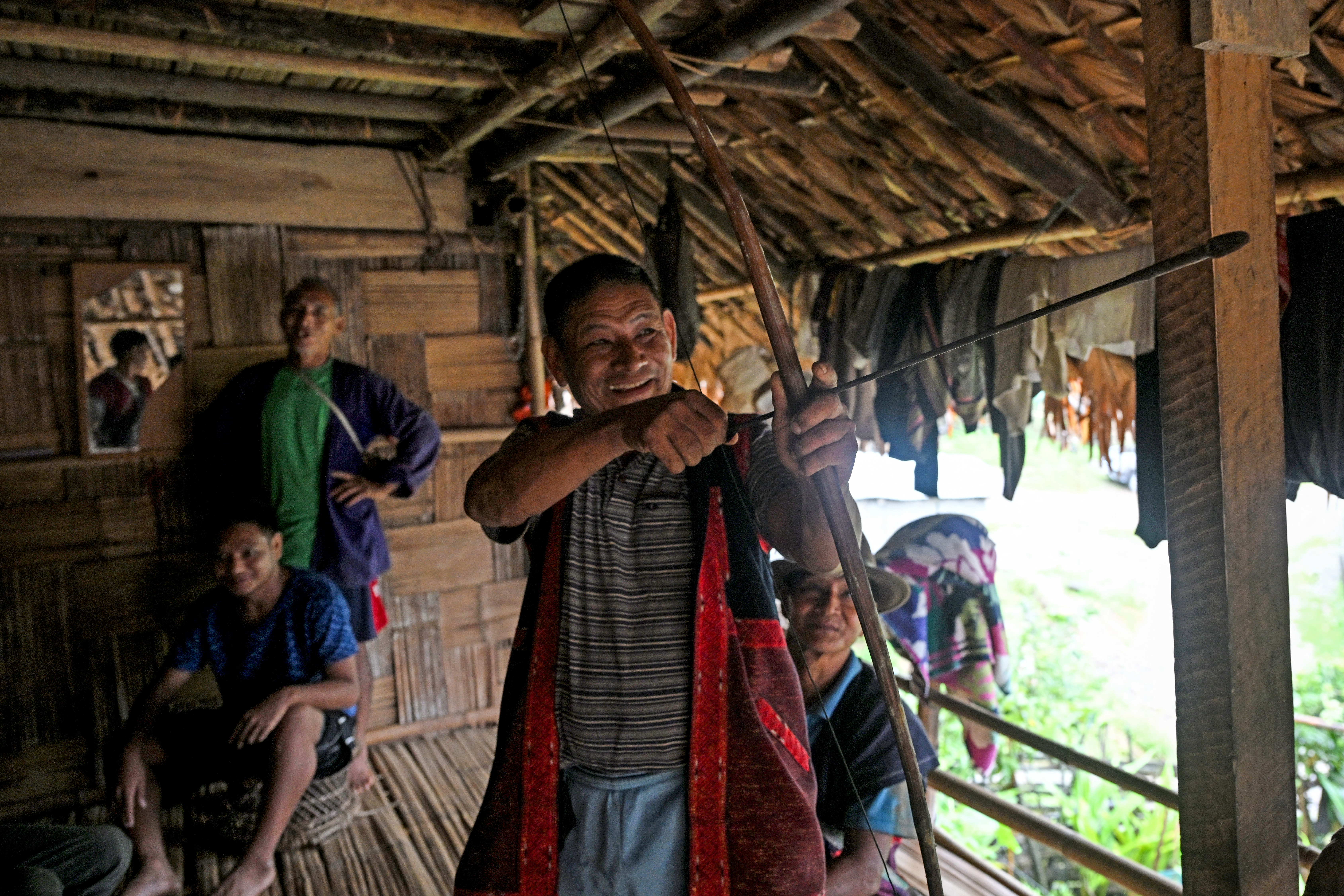 This photograph taken on August 21, 2025 shows a man from the Adi tribe gesturing with a bow and arrow at his house facing potential risk of submersion owing to the Siang Upper Multipurpose Project (SUMP) on the Siang river, a proposed hydroelectric mega-dam project, at Riew village in the East Siang district of the northeastern state of Arunachal Pradesh. On a football field ringed by misty mountains, the air rang with fiery speeches as tribesmen protested a planned mega-dam -- India's latest move in its contest with China over Himalayan water. (Photo by Arun SANKAR / AFP) / TO GO WITH 'INDIA-CHINA-WATER-ENVIRONMENT', FOCUS BY ARUNABH SAIKIA