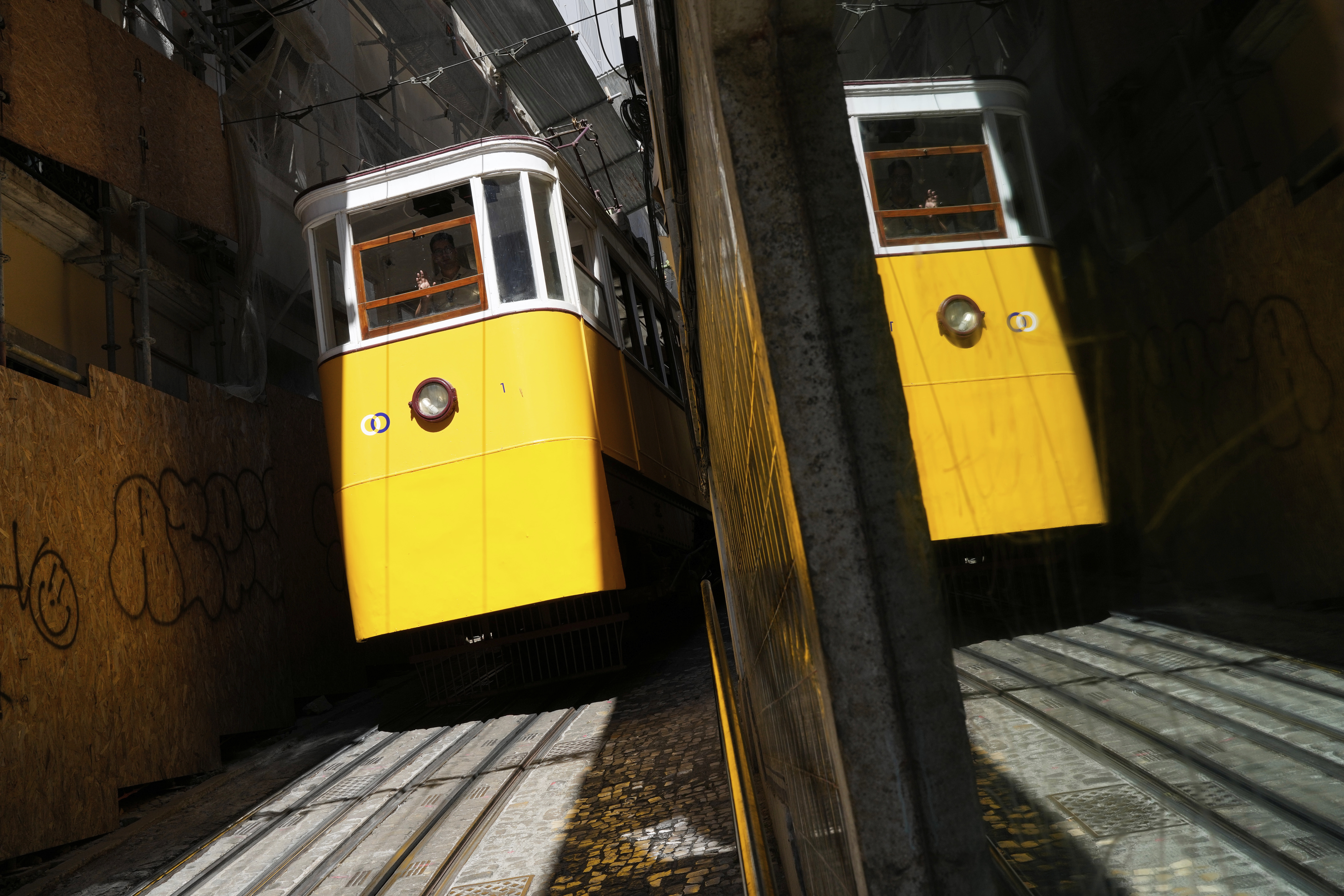The driver of the Lavra funicular waves while steering it downhill through a narrow street to downtown Lisbon