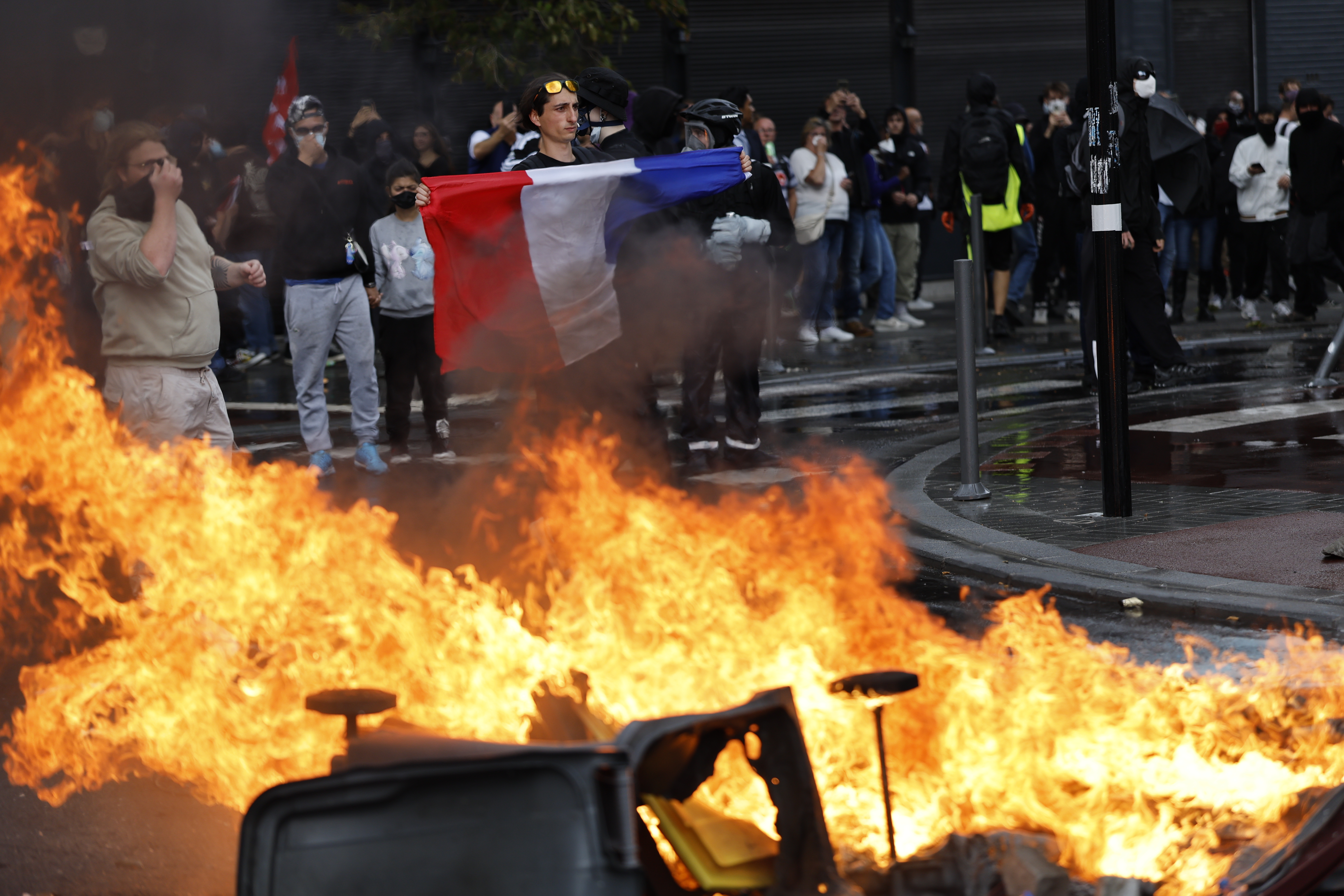 A protester displays a French national flag next to burning rubbish bins.