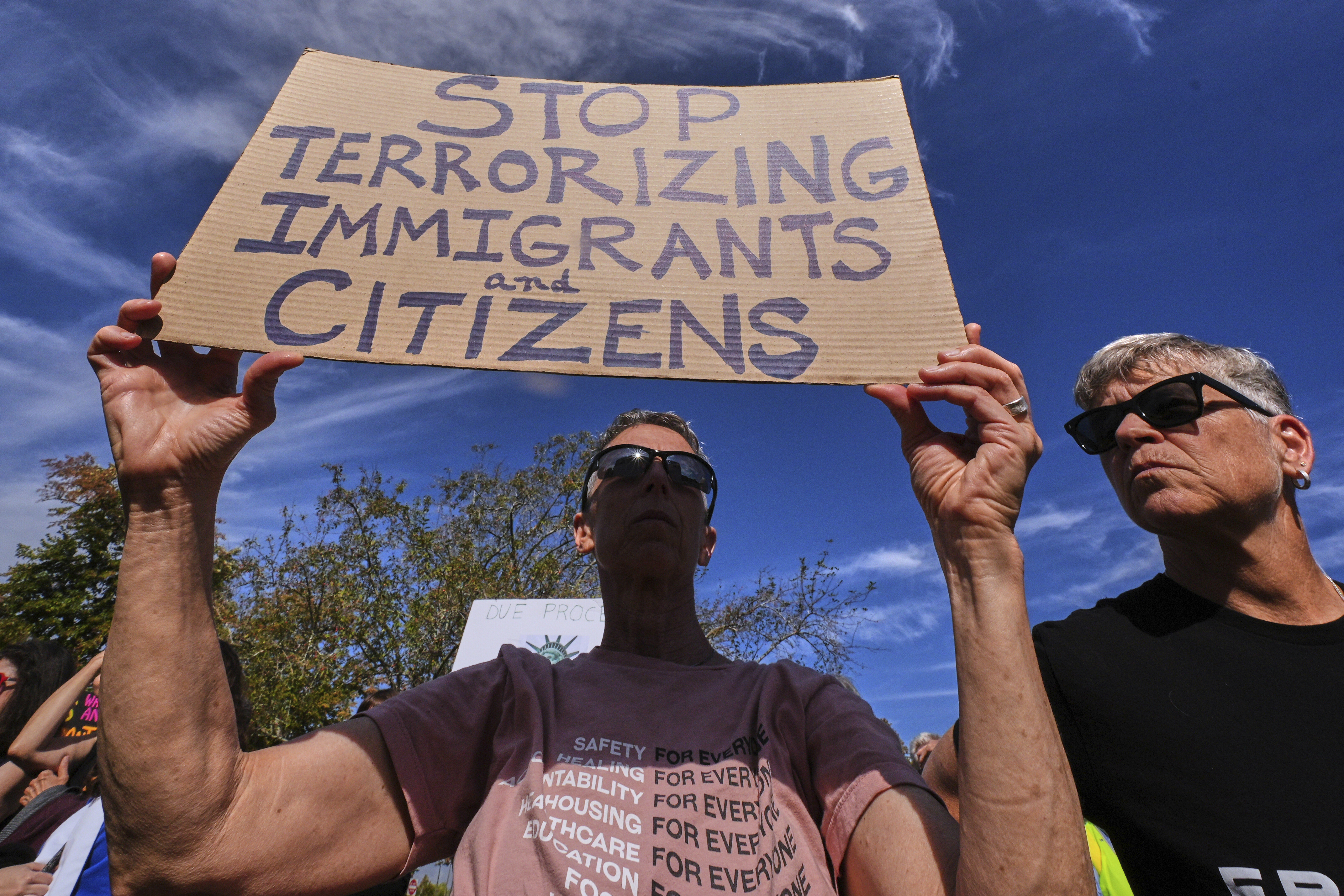 A protester holds a banner that reads 'Stop Terrorizing Immigrants and Citizens'.