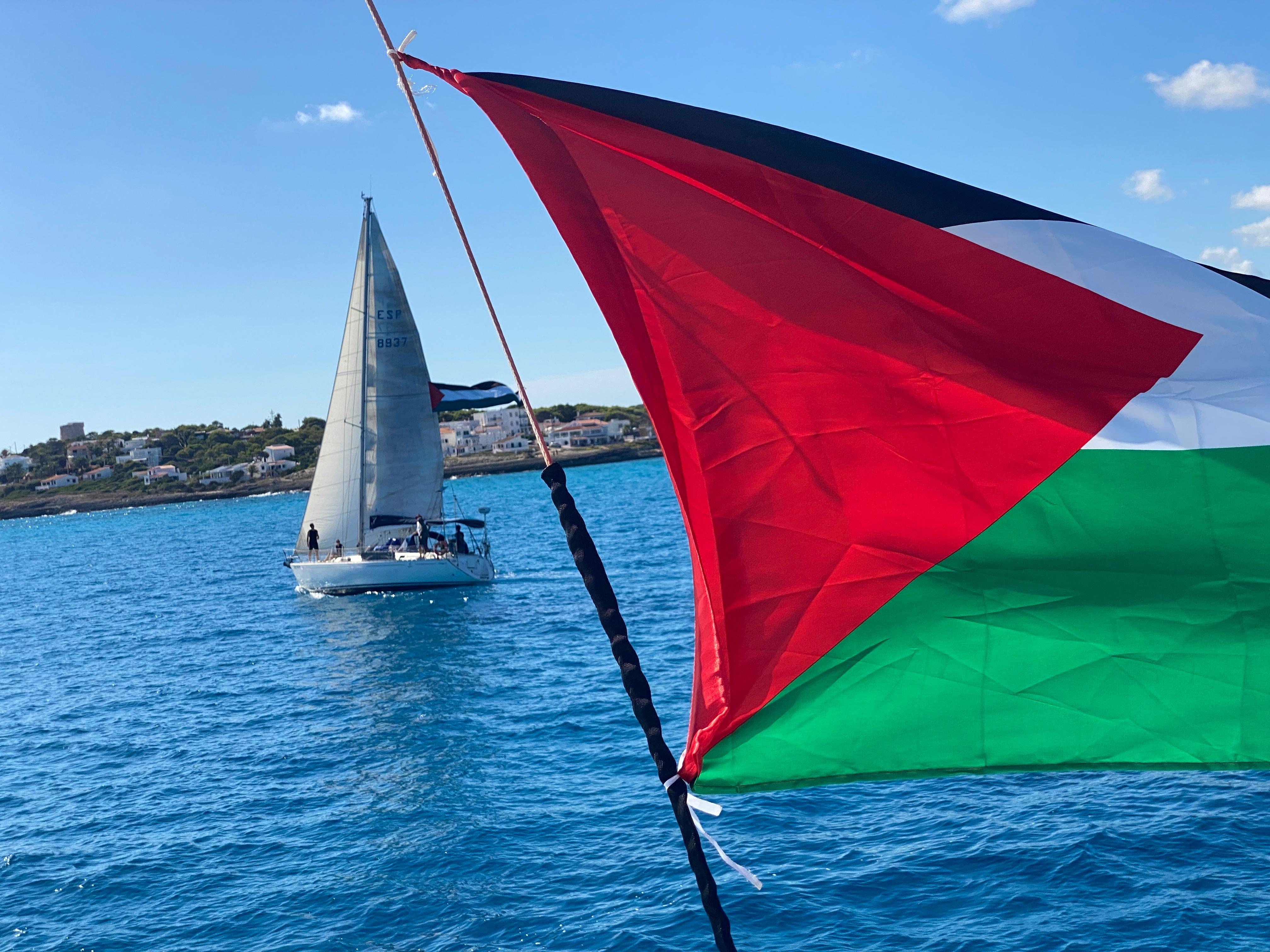 A Palestinian flag in front of a yacht in the sea