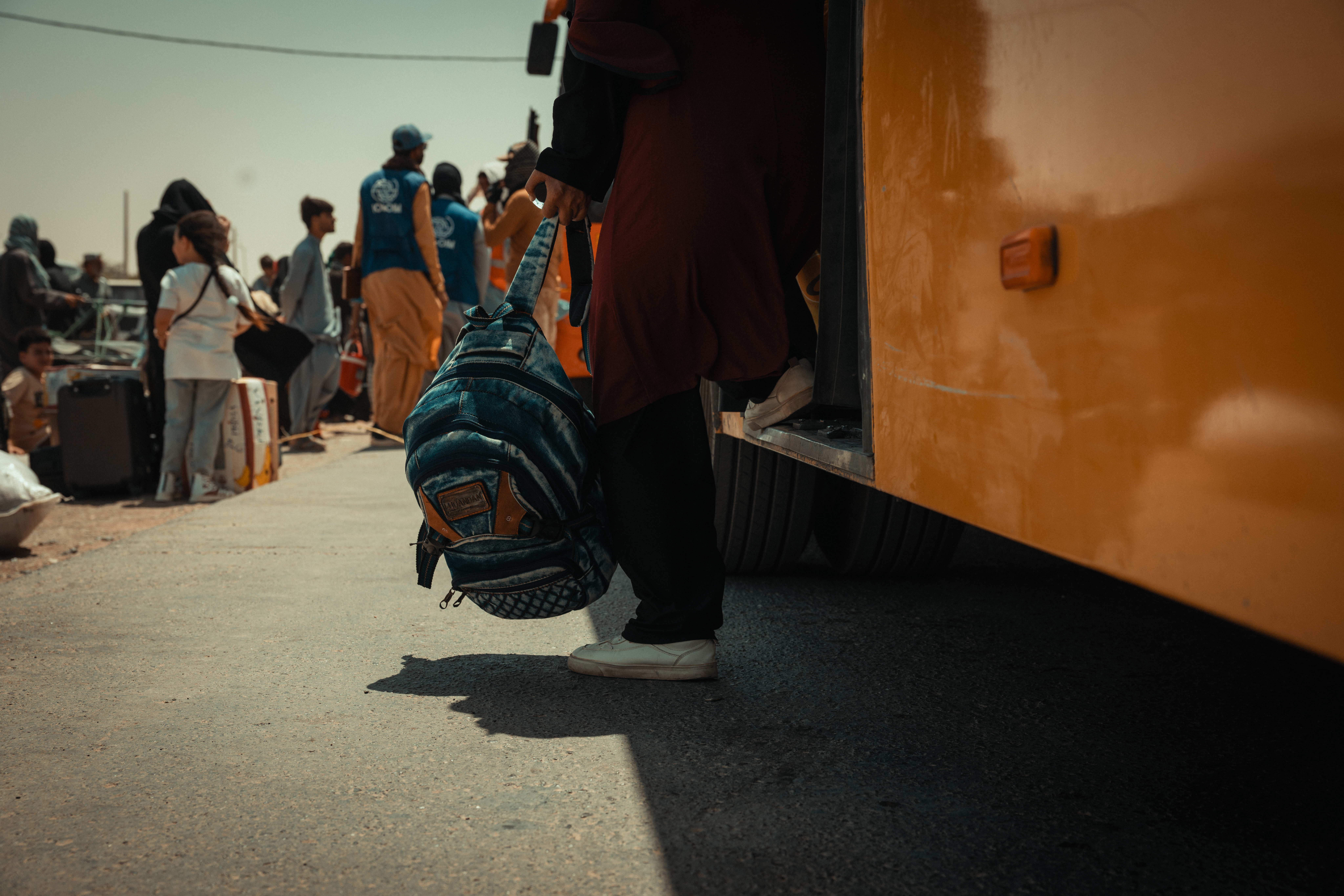 At the Islam Qala border, a woman takes her first steps off the bus onto Afghan soil. Photo: IOM 2025/Mohammad Osman Azizi