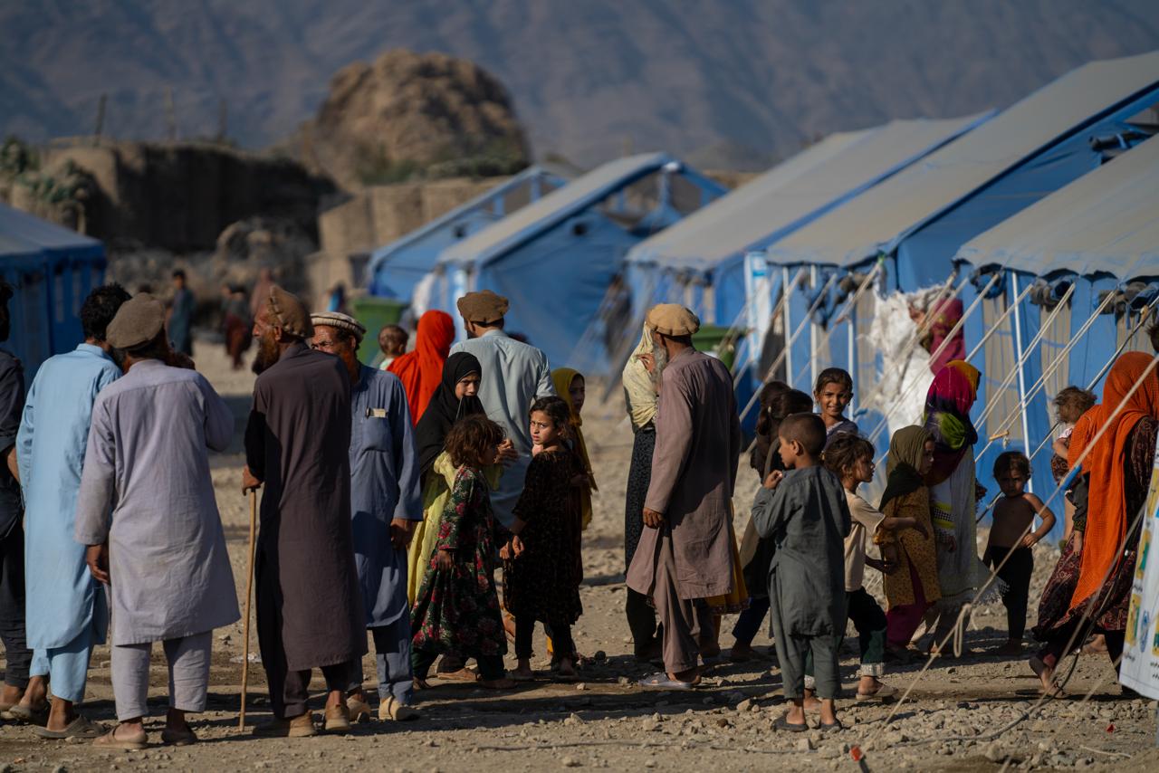 People walk in a displacement camp lined with tents.