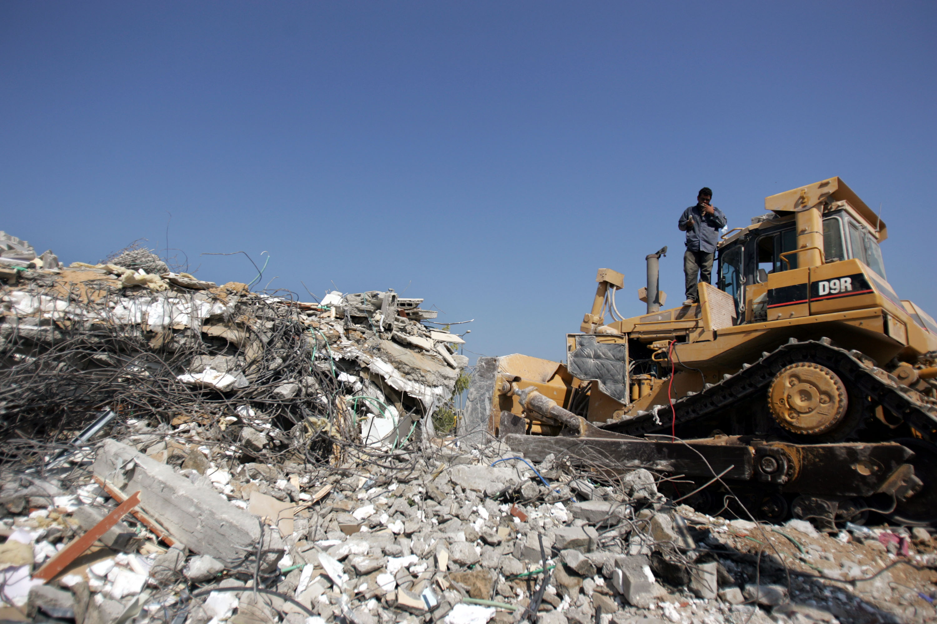 KFAR DAROM, GAZA STRIP - AUGUST 30: A bulldozer demolishes houses on August 30, 2005 in the Kfar Darom settlement in the Gaza Strip. After the Israeli pullout from Gaza which removed about 9,000 Jewish settlers from 21 settlements in Gaza and four in the northern West Bank, the Israeli Army is now demolishing all the settlements and is expected to leave the Gaza Strip in the coming weeks. (Photo by Marco Di Lauro/Getty Images)