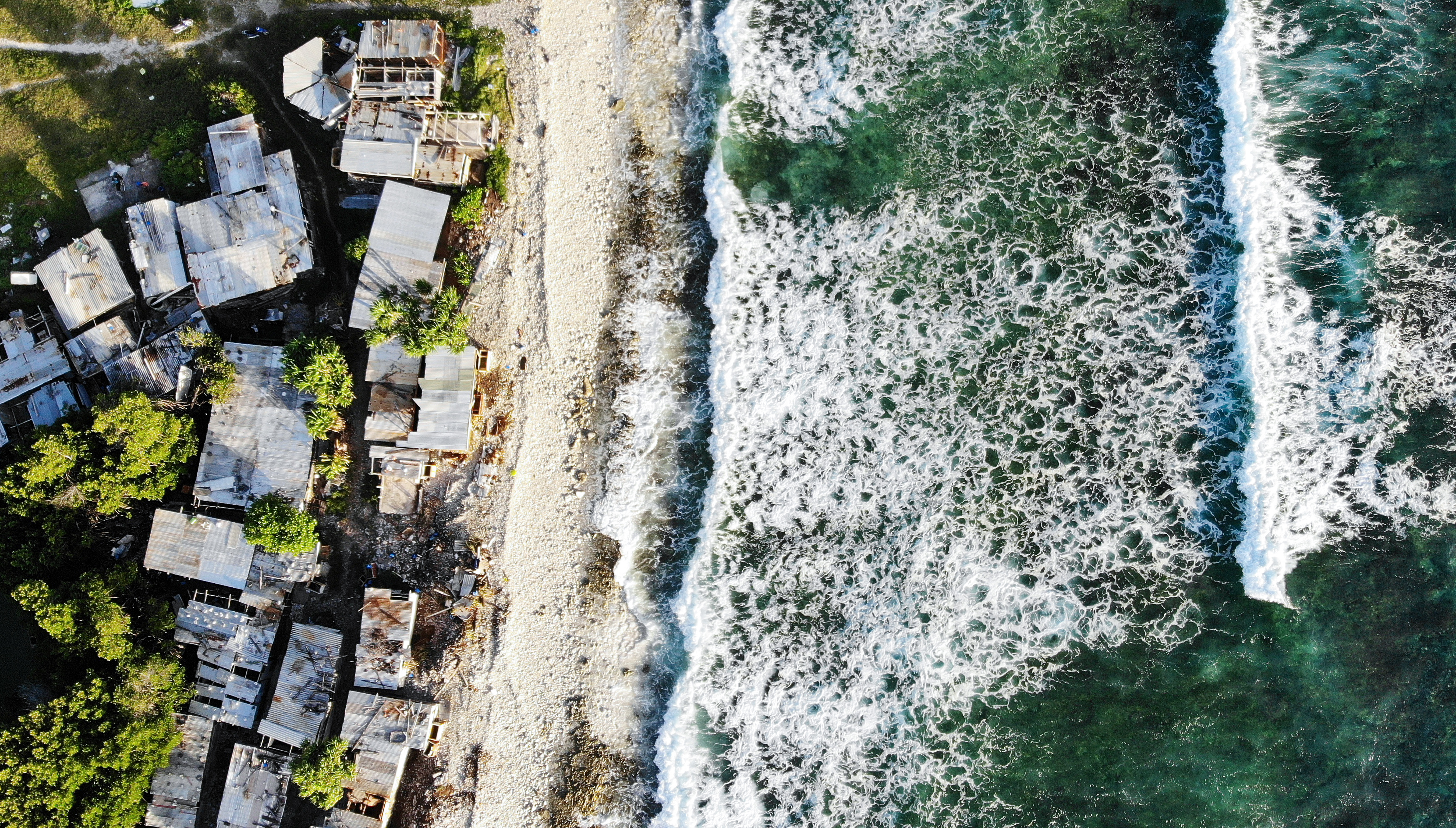 FUNAFUTI, TUVALU - NOVEMBER 28: An aerial view of homes next to the Pacific Ocean on November 28, 2019 in Funafuti, Tuvalu. The low-lying South Pacific island nation of about 11,000 people has been classified as ‘extremely vulnerable’ to climate change by the United Nations Development Programme. The world’s fourth-smallest country is struggling to cope with climate change related impacts including five millimeter per year sea level rise (above the global average), tidal and wave driven flooding, storm surges, rising temperatures, saltwater intrusion and coastal erosion on its nine coral atolls and islands, the highest of which rises about 15 feet above sea level. In addition, the severity of cyclones and droughts in the Pacific Island region are forecast to increase due to global warming. Some scientists have predicted that Tuvalu could become inundated and uninhabitable in 50 to 100 years or less if sea level rise continues. The country is working toward a goal of 100 percent renewable power generation by 2025 in an effort to curb pollution and set an example for larger nations. Tuvalu is also exploring a plan to build an artificial island. (Photo by Mario Tama/Getty Images)