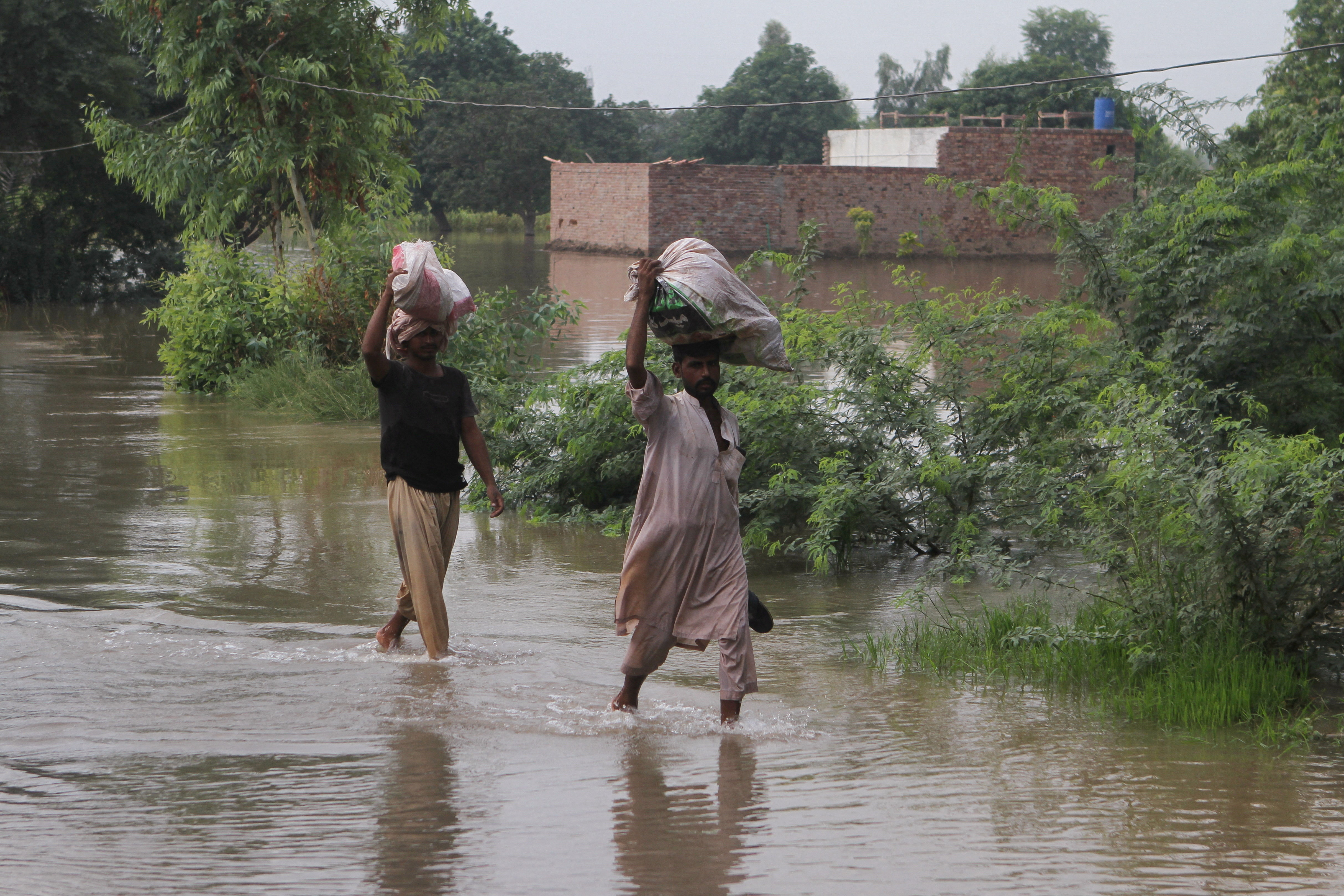 Residents carry their belongings as they wade through a flooded area in Muzaffargarh, Pakistan