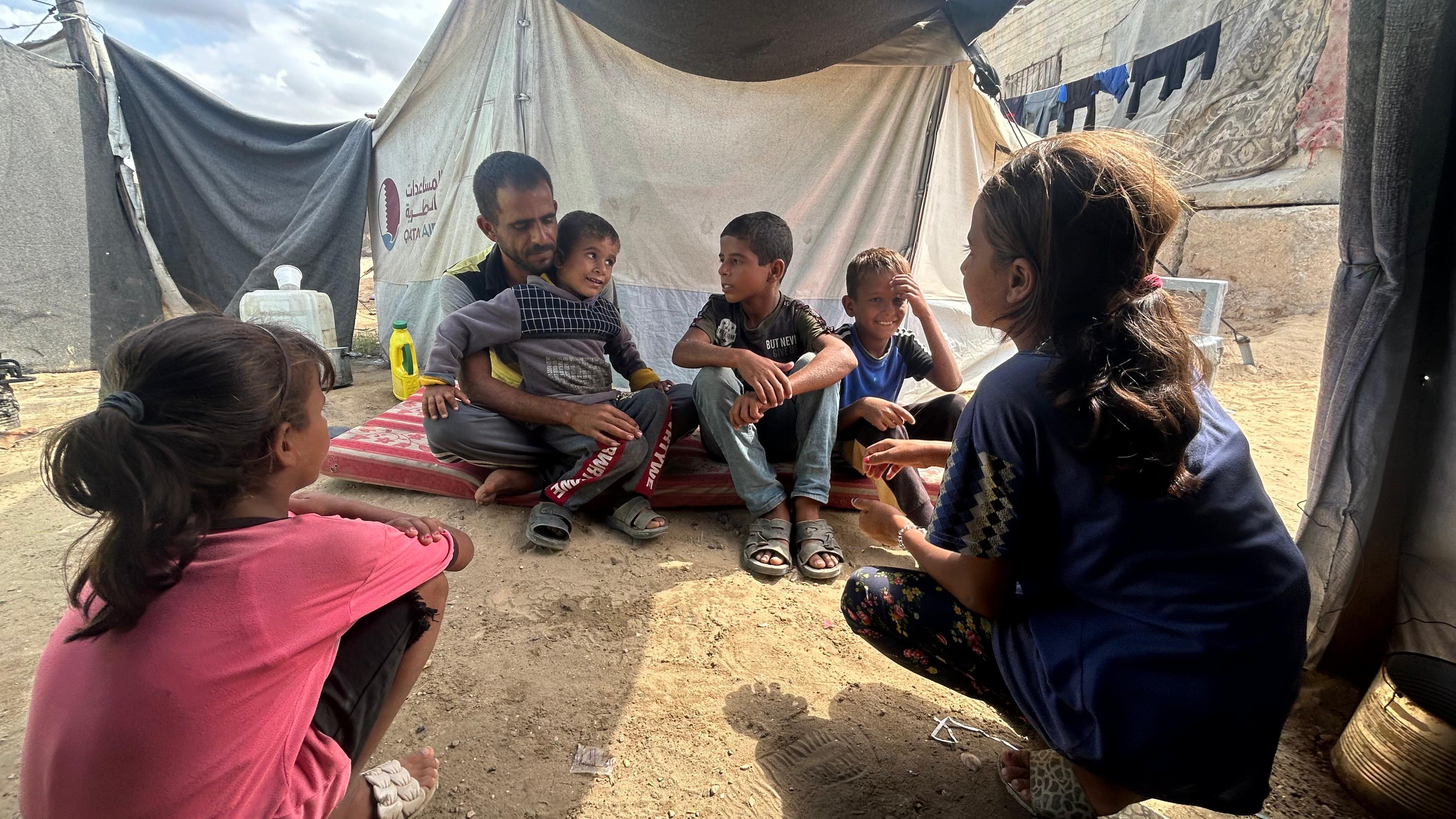 Omar al-Dadda sits with his children outside their makeshift shelter in Al-Mawasi whilewaiting for food aid to arrive