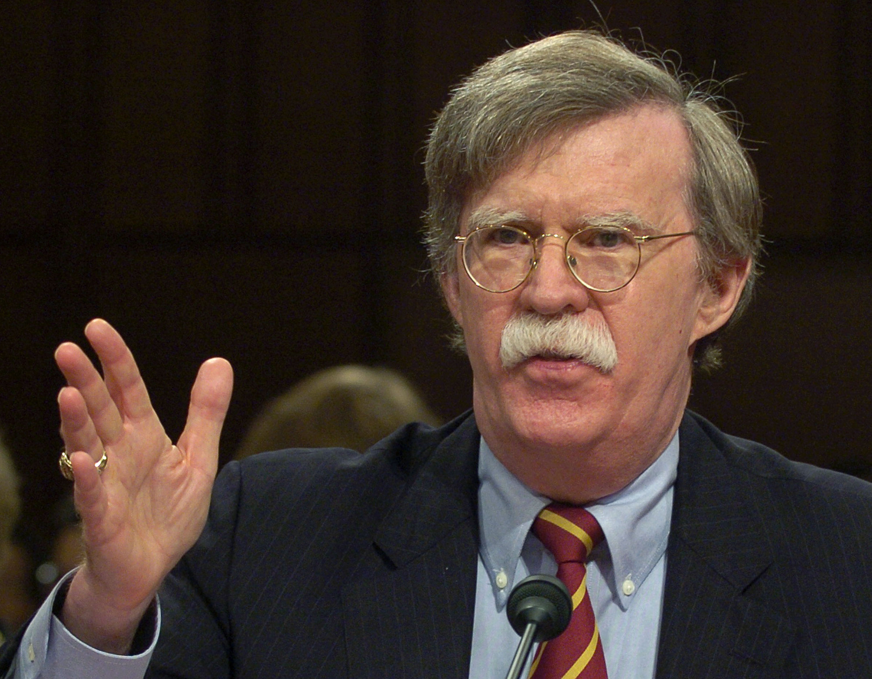 John Bolton testifies, raising his hand as he speaks.