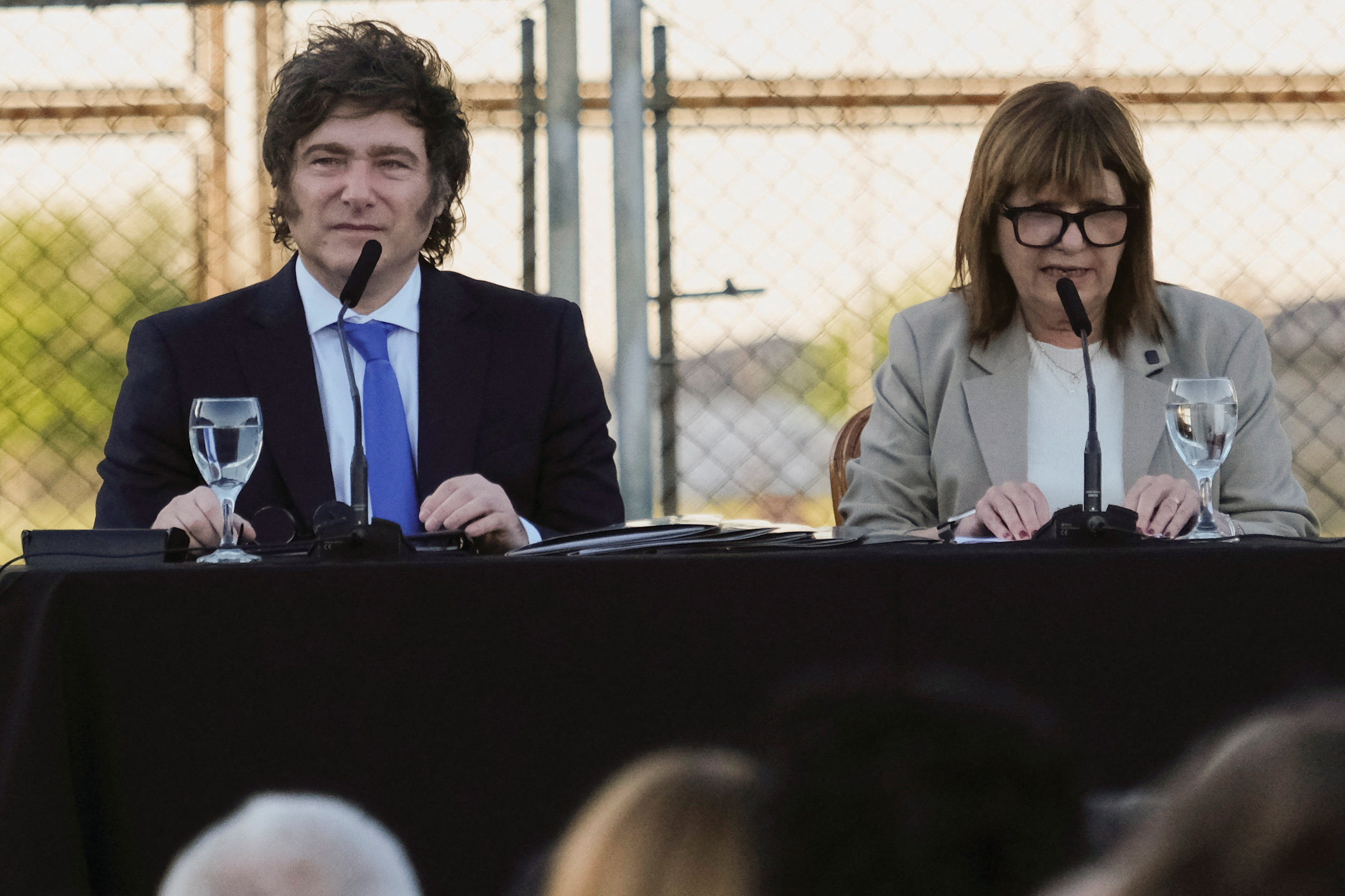Javier Milei and Patricia Bullrich sit at a table at an outdoor event.