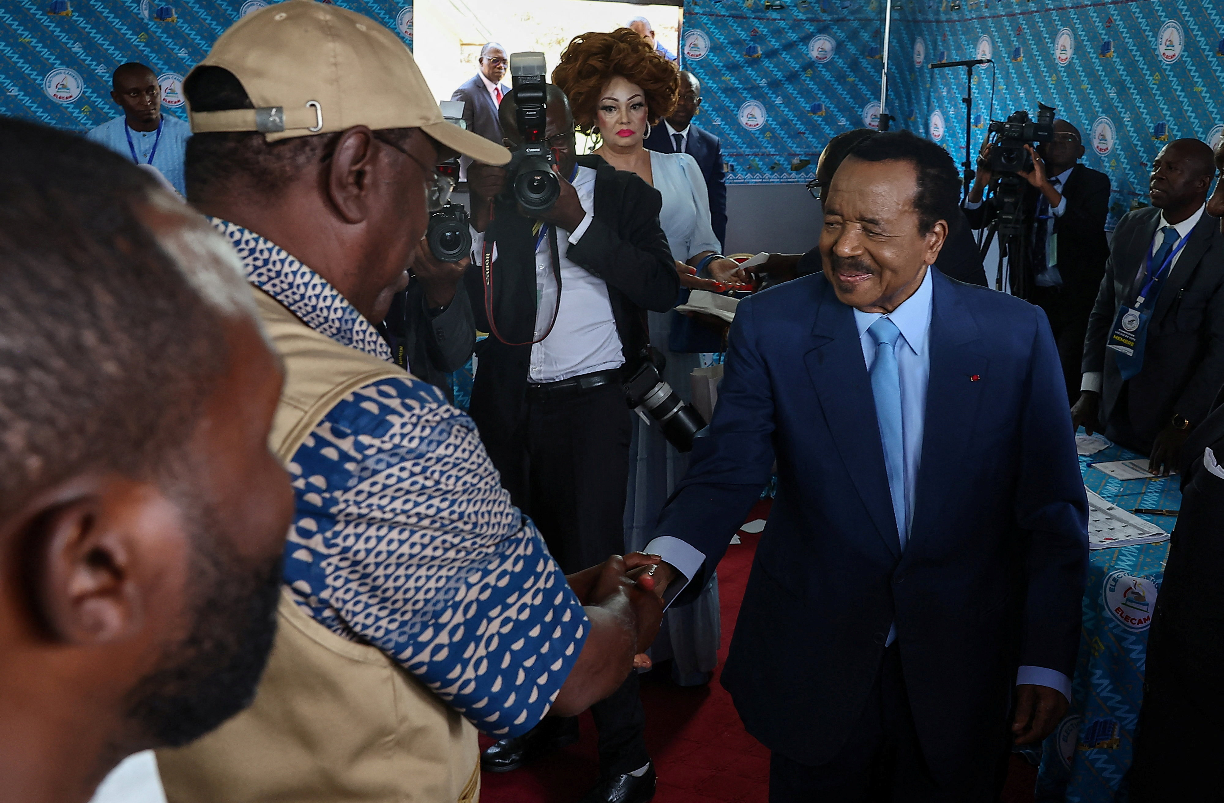 Cameroonian President Paul Biya, 92, who is seeking an eighth term shakes hands with election observer after he casted his ballot while his wife Chantal looks on, during the presidential election in Yaounde, Cameroon