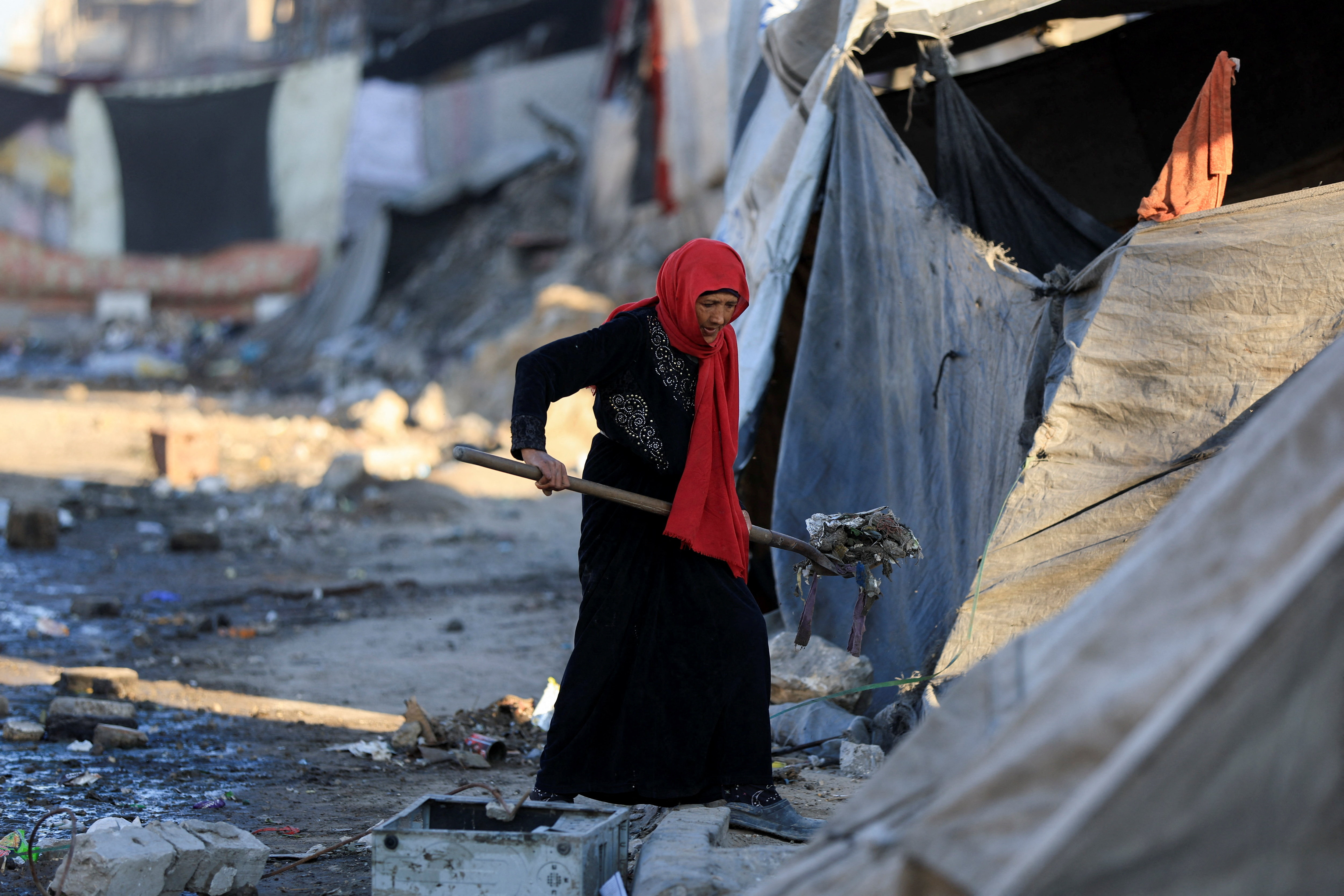 A Palestinian woman cleans an area next to tents, amid a ceasefire between Israel and Hamas, in Gaza City, October 14, 2025