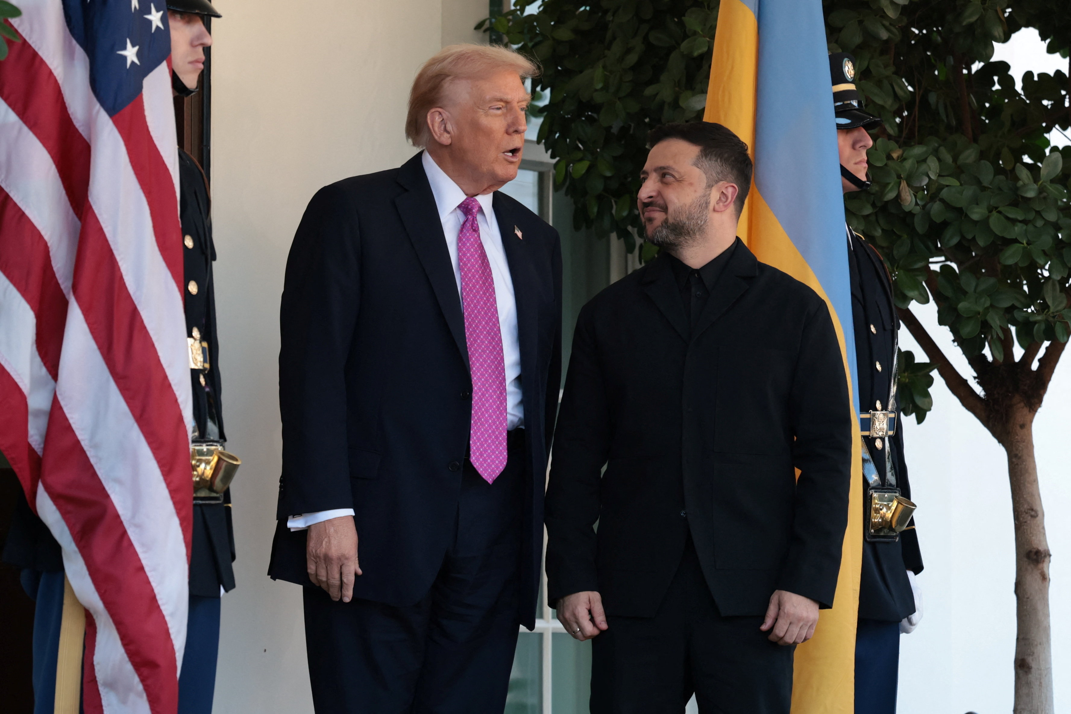 Zelenskyy, dressed in a black suit, looks at Trump