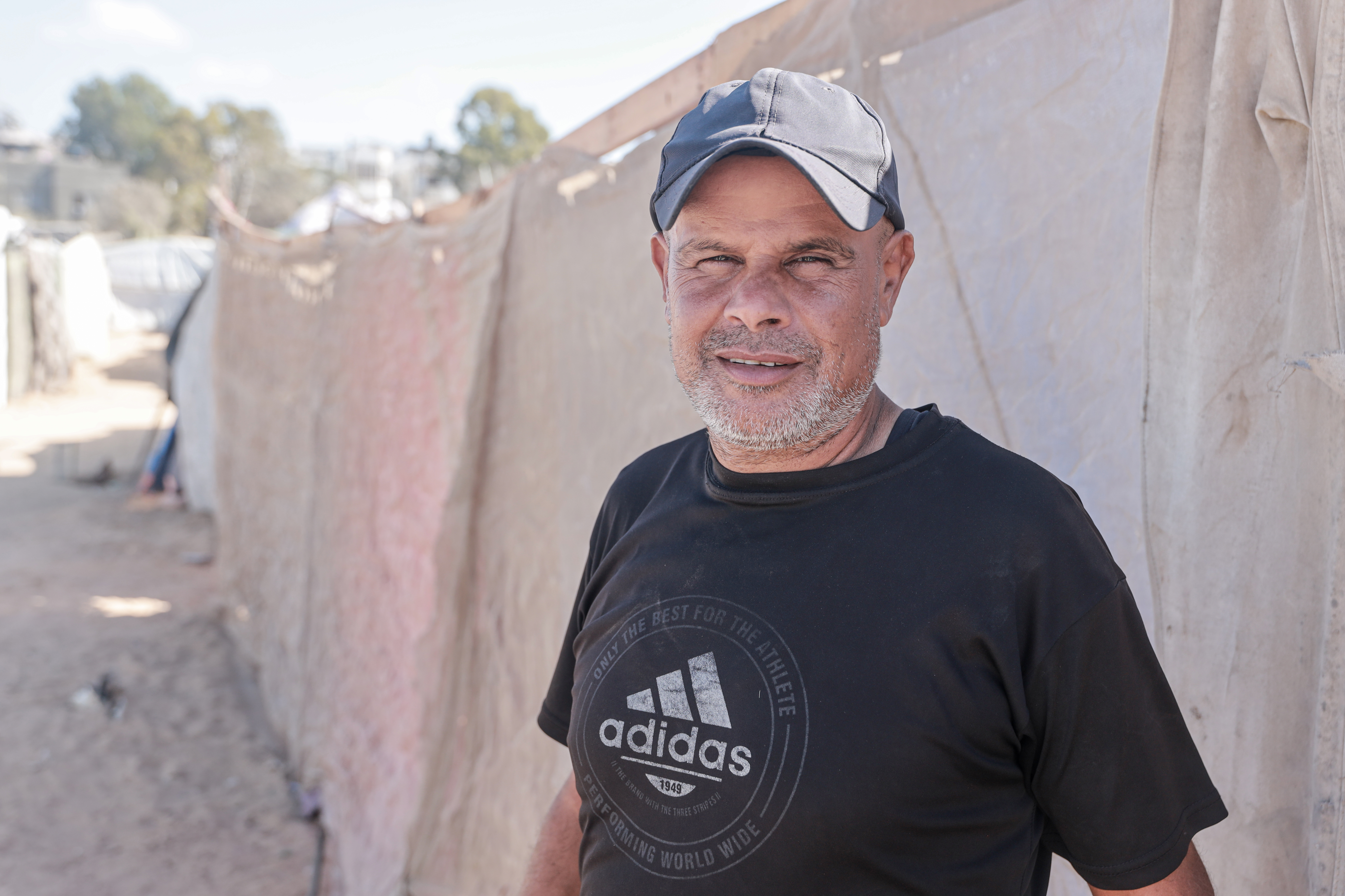A man, prematurely greying, squints tiredly at the camera from under the bill of his cap