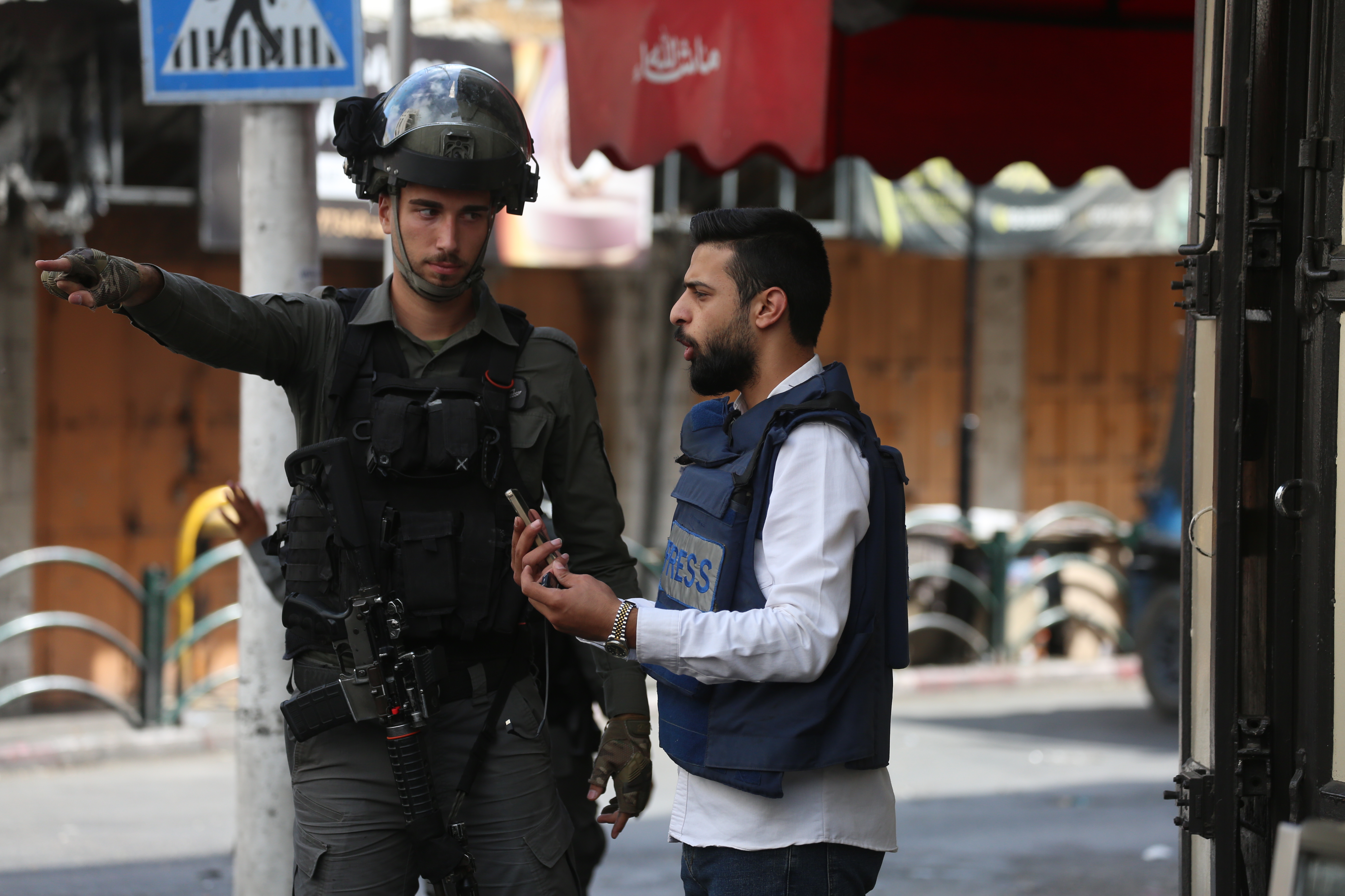 Journalist in press vest talks to a soldier pointing