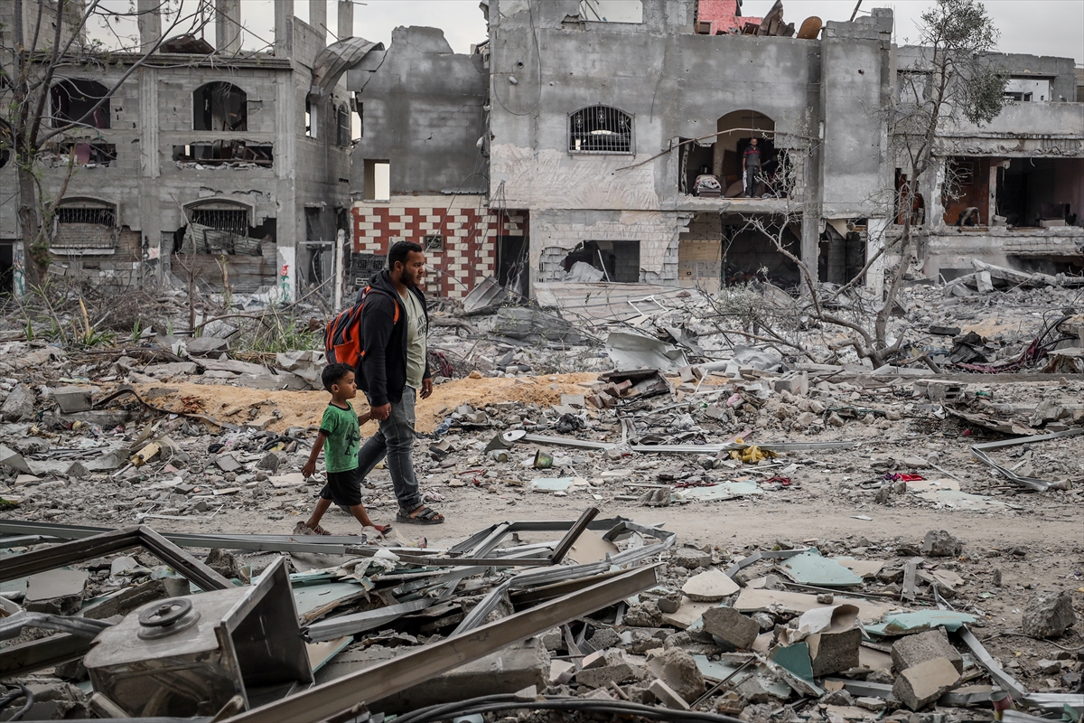 people walk past concrete buildings that have been reduced to rubble