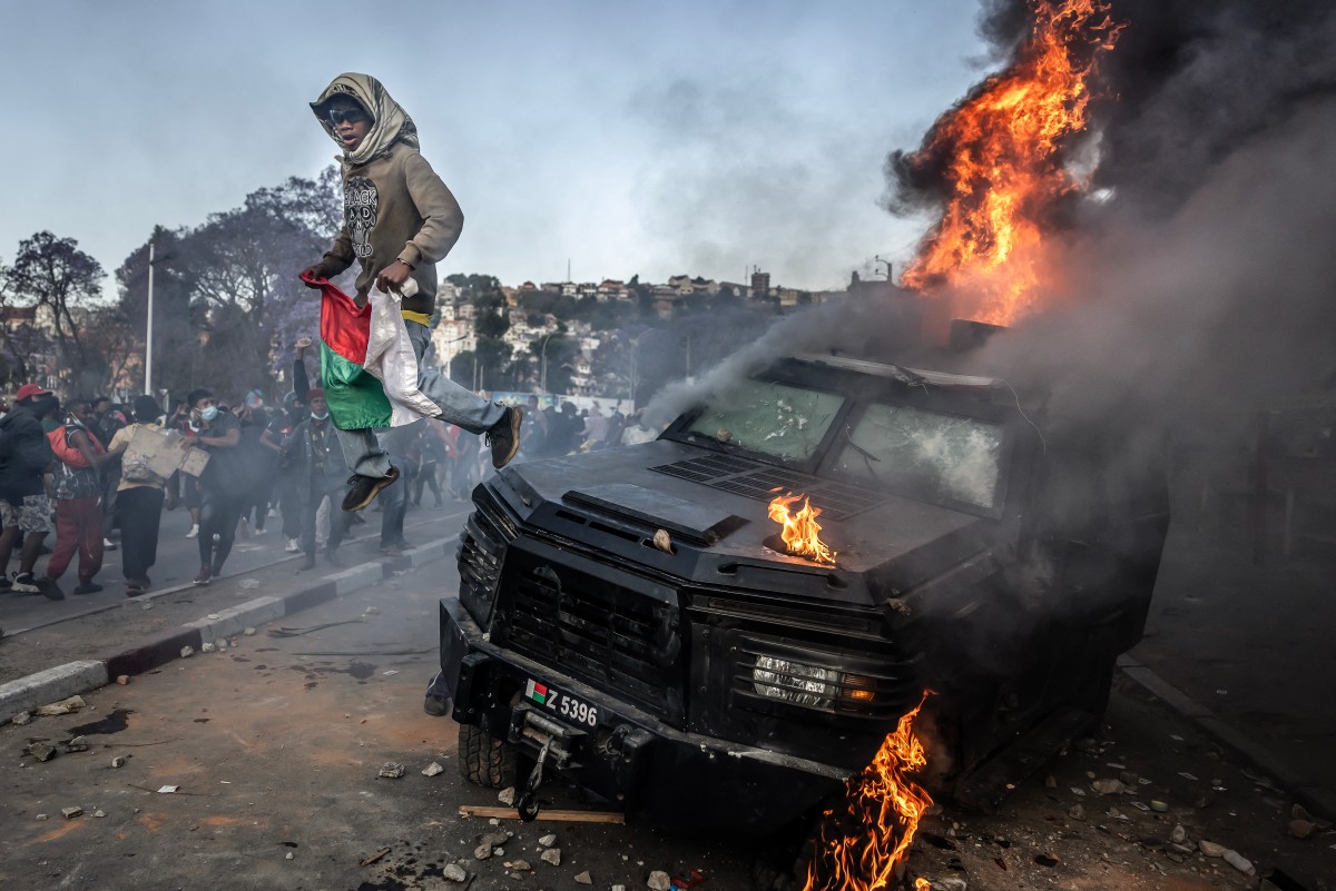 A protester holding a Malagasy flag jumps from a vandalised Gendarmerie armoured vehicle