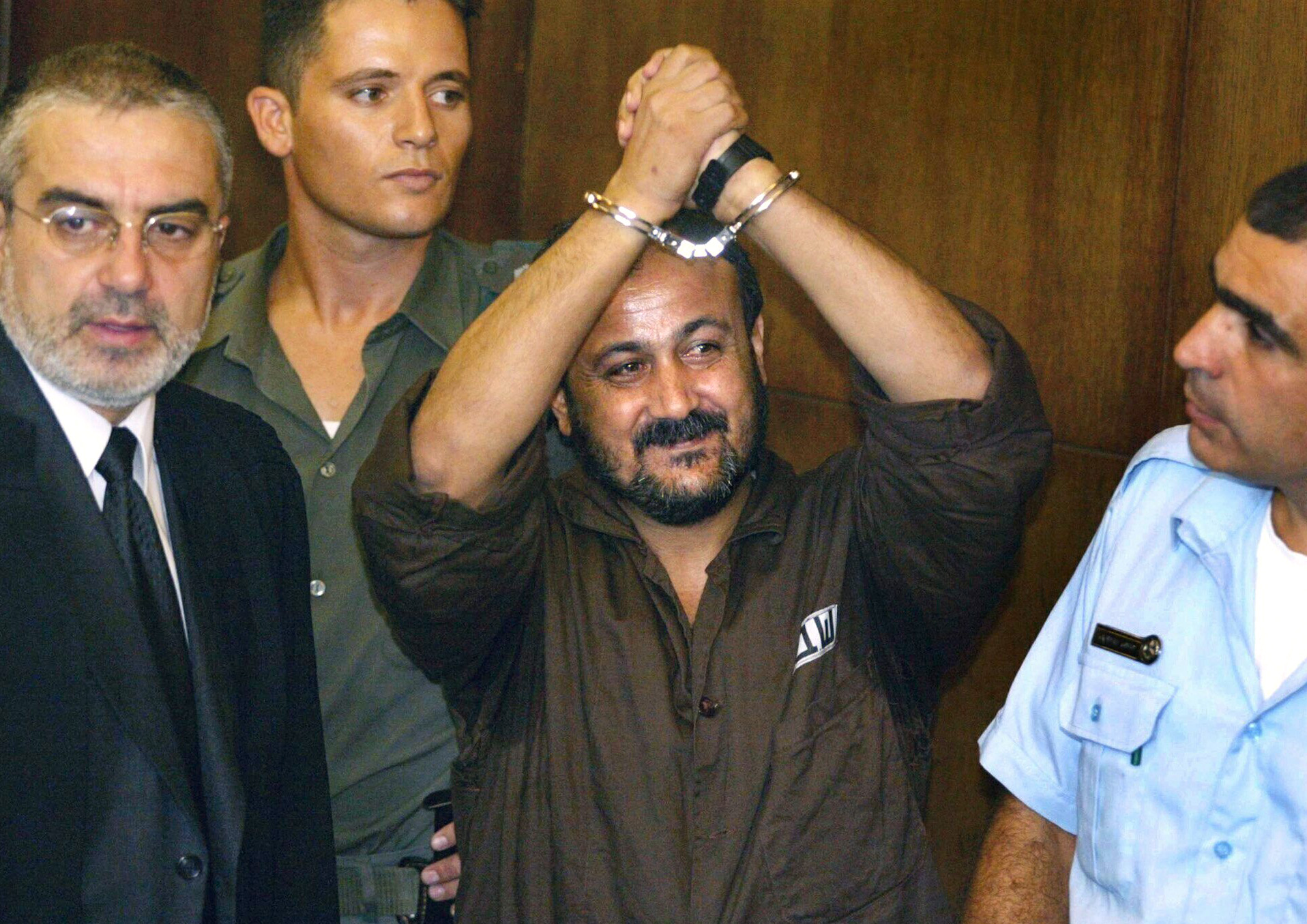 FILE - Marwan Barghouti, center, raises his handcuffed hands in the air on the opening day of his trial in Tel Aviv, Israel, Aug. 14, 2002. [Brennan Linsley/AP Photo]