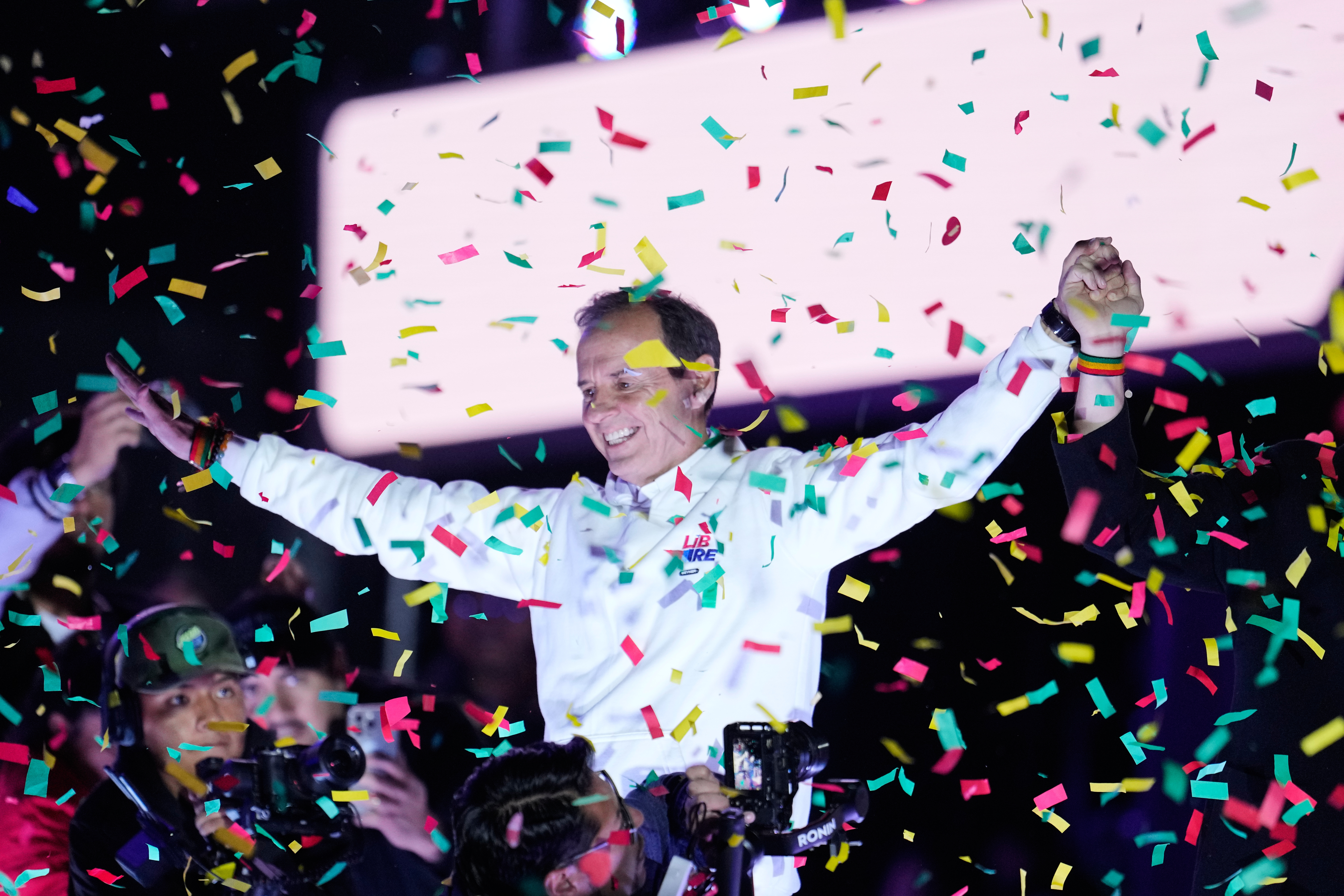 Jorge Quiroga spreads out his arms on stage at a rally as confetti falls.