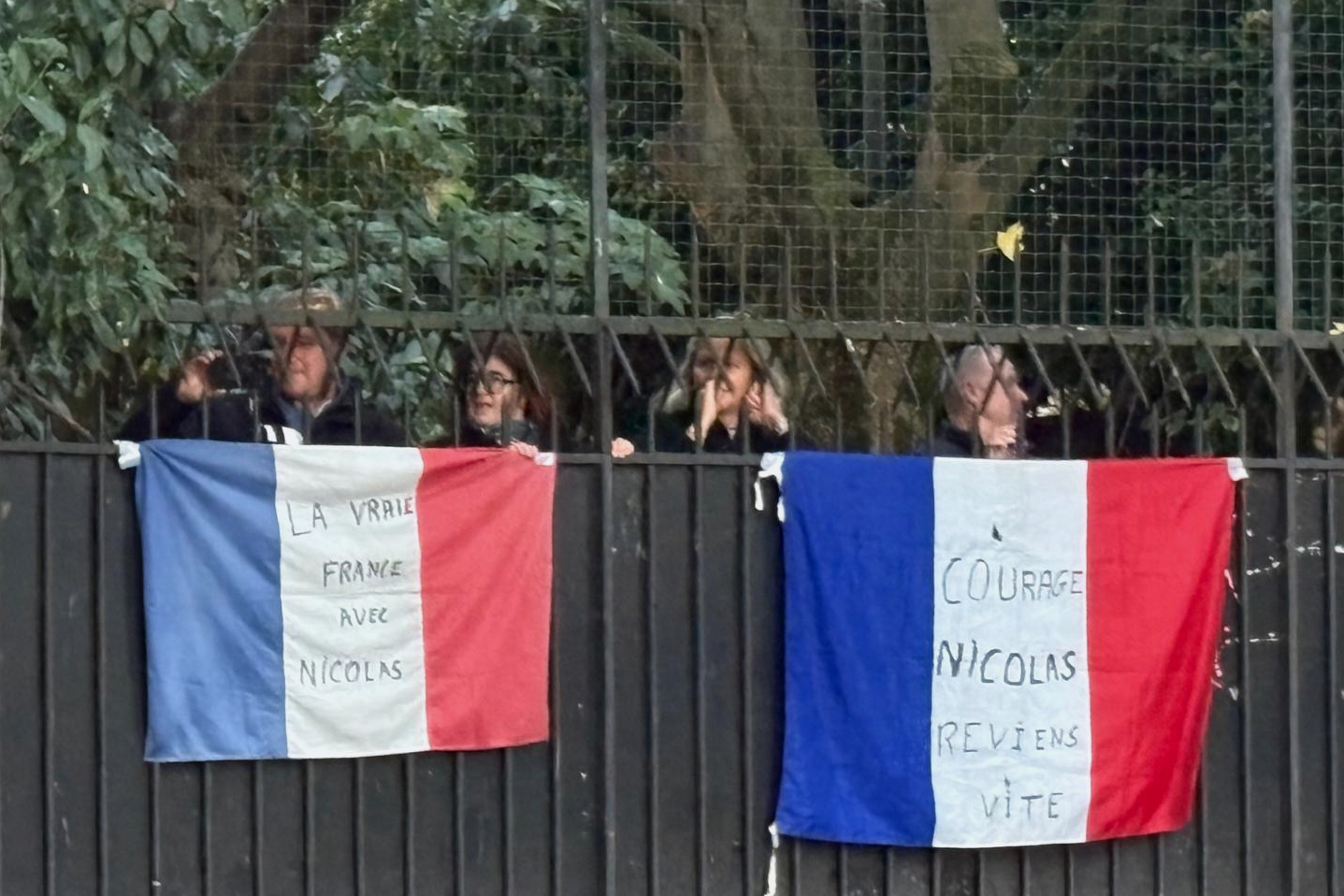 People stand behind French flags with inscription reading "Courage Nicolas, come back soon", right, and "True France with Nicolas" outside former French President Nicolas Sarkozy's home, Tuesday, Oct. 21, 2025 in Paris. Former French President Nicolas Sarkozy heads to prison to serve time for a criminal conspiracy to finance his 2007 election campaign with funds from Libya. (AP Photo/Masha Macpherson)