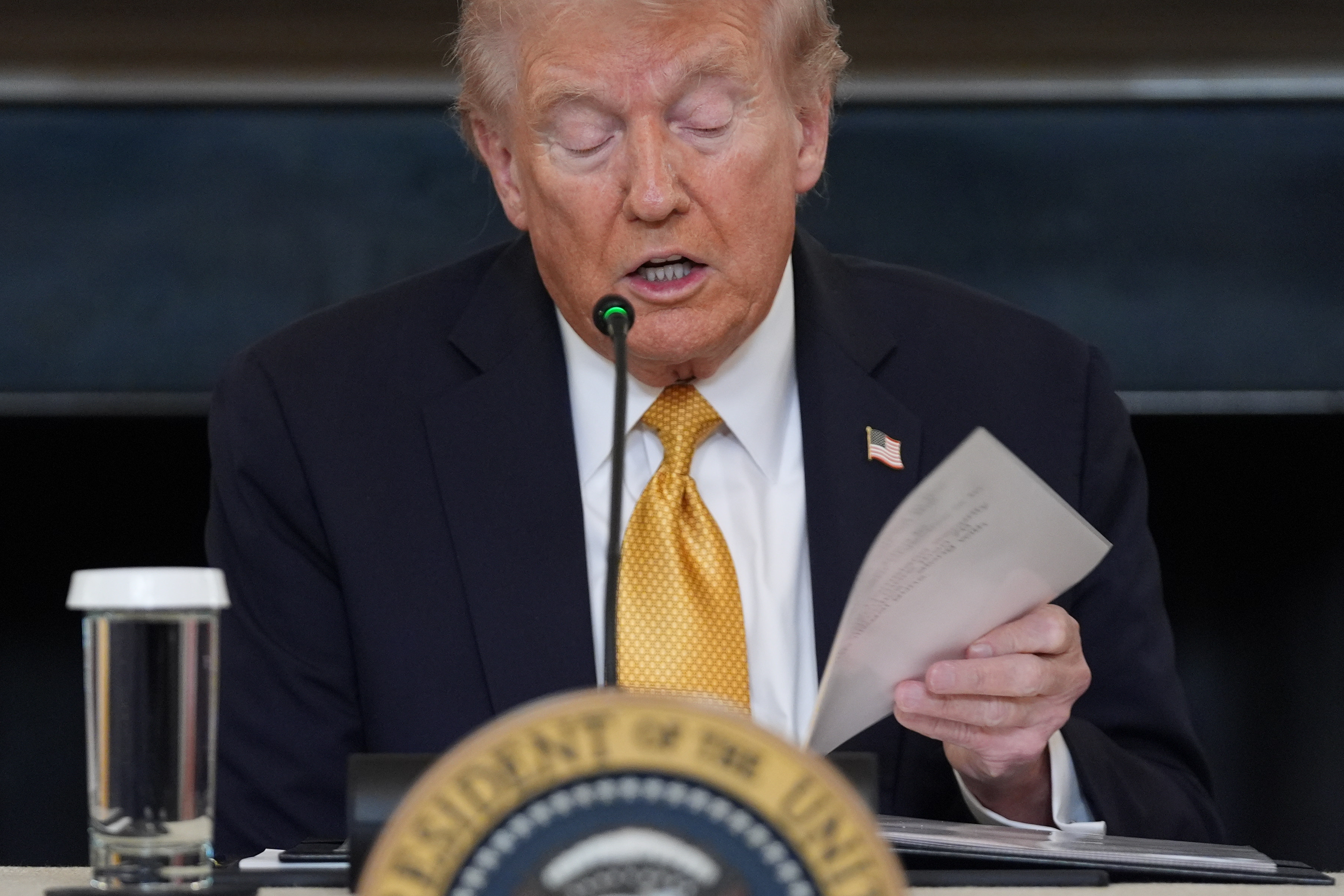 Donald Trump at a panel, thumbing through papers.