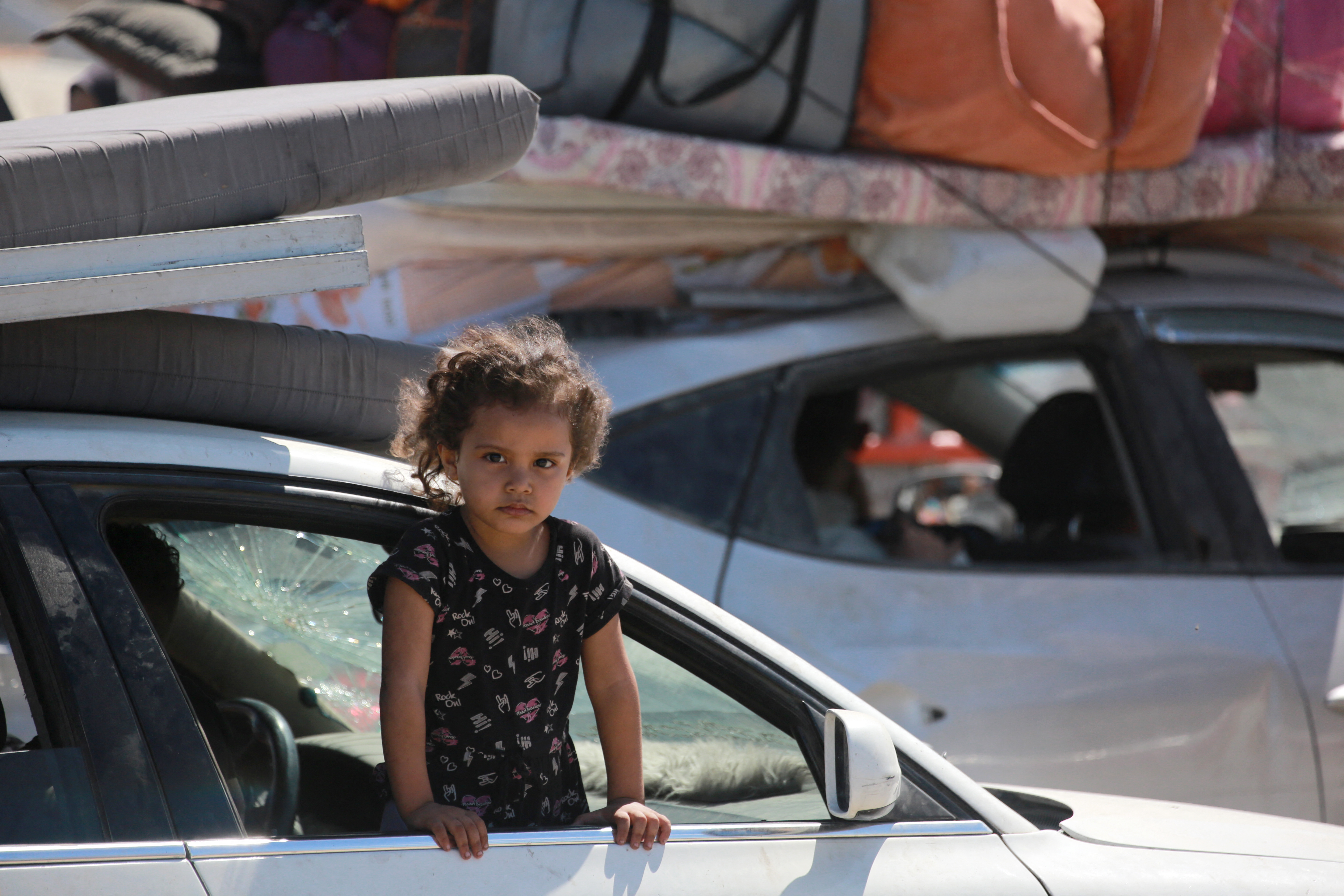 A girl looks out a car window while Palestinians carrying belongings arrive on a coastal path northwest of Nuseirat refugee camp as they are displaced southward from Wadi Gaza following an Israeli announcement of closing Al-Rashid road towards the north of the besieged Gaza Strip on October 1, 2025.