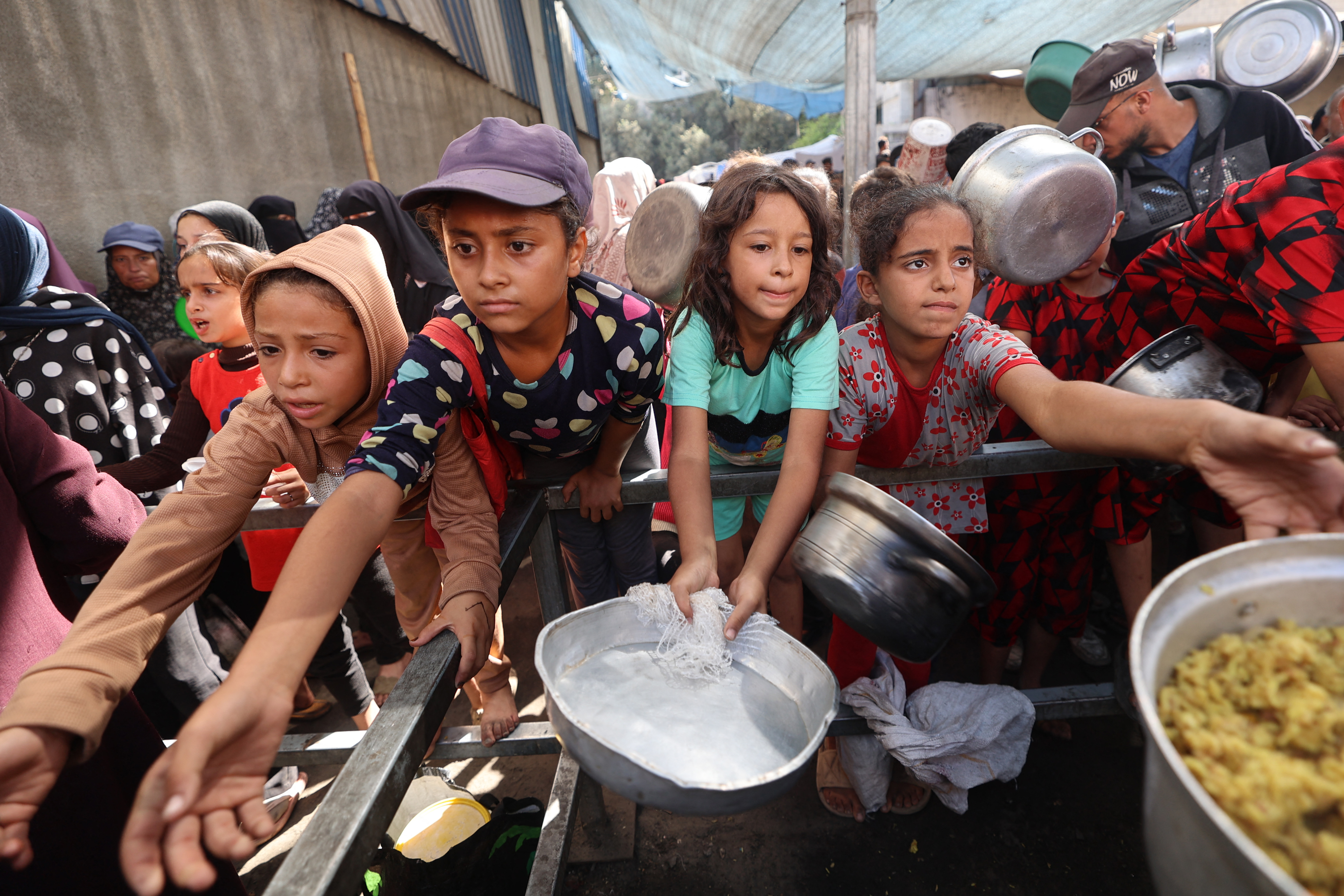 Palestinian children gather to receive food portions from a charity kitchen in the Nuseirat refugee camp, located in the central Gaza Strip, on October 21, 2025, a week after a ceasefire came into effect.