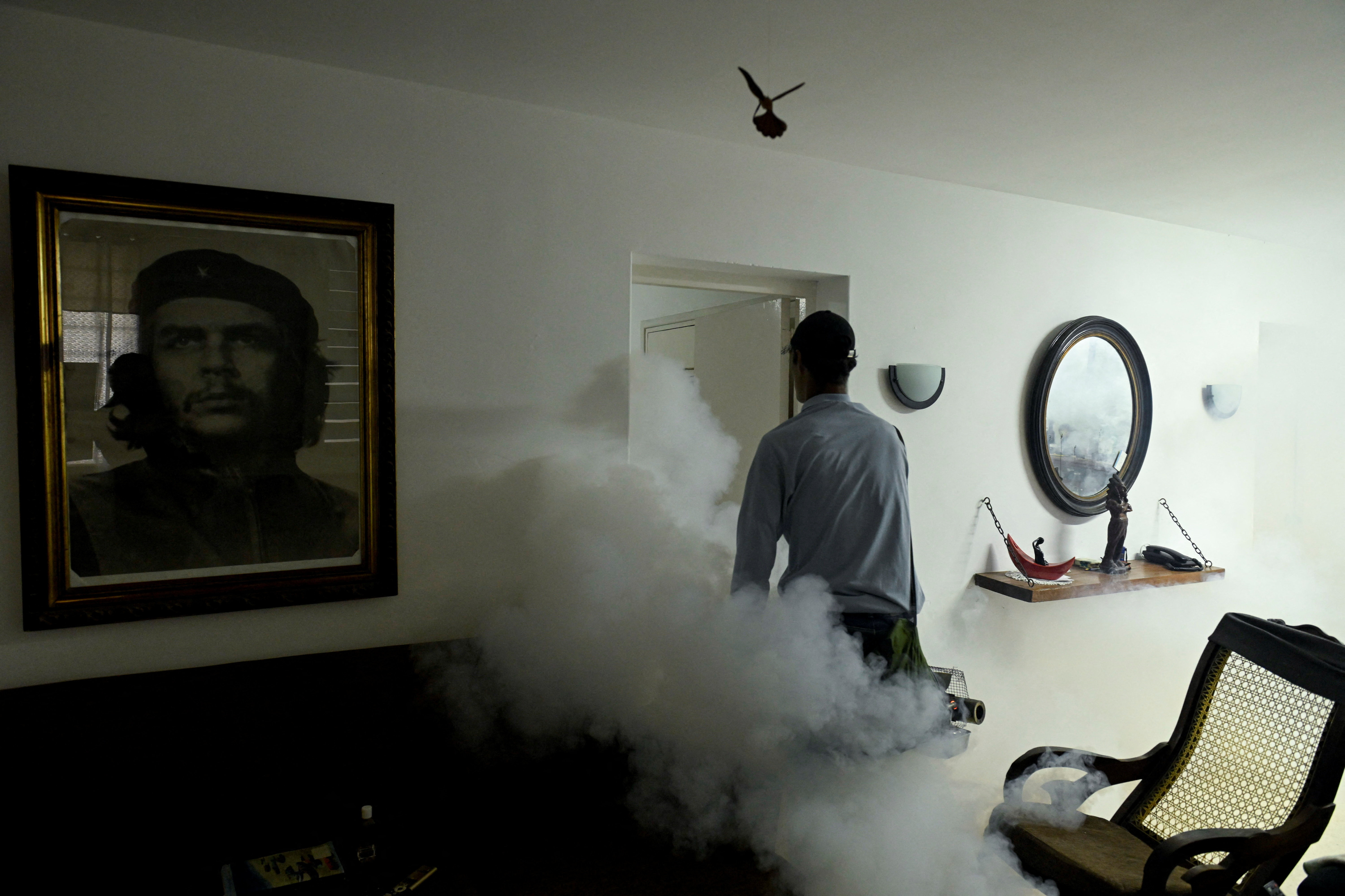 State worker Carlos Gutierrez uses a fogging machine to fumigate inside a house, beside an image of late revolutionary hero Che Guevara as part of a public health campaign against the spread of mosquito-transmitted virus that causes Chikungunya, in Havana, Cuba November 13, 2025. REUTERS/Norlys Perez