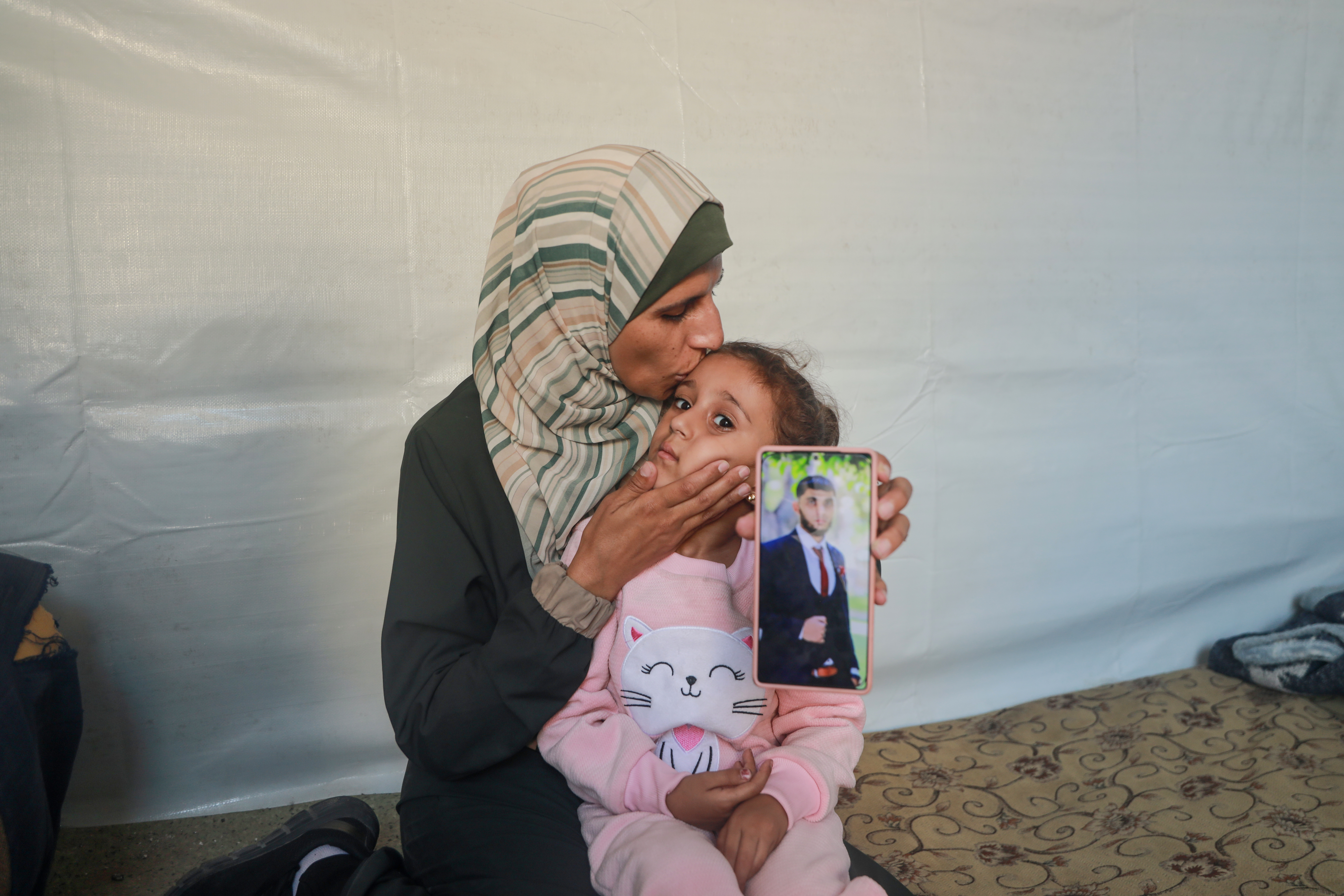 Israa al-Areer kisses her daugher as she holds up a mobile phone showing a picture of her husband Yasser