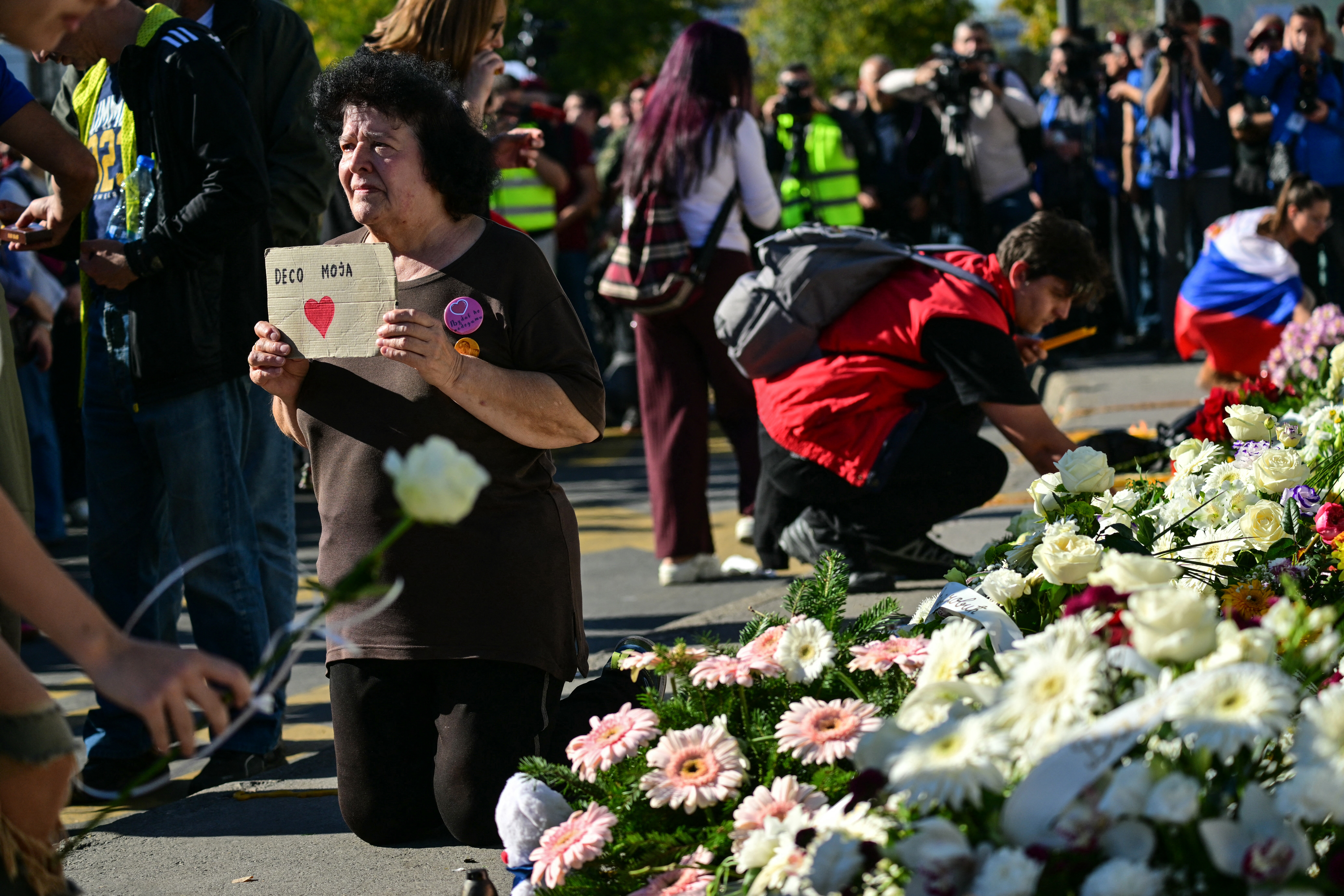 A woman holds a sign with a heart and reading "My children" as mourners lay flowers during a gathering marking the first anniversary of the Novi Sad railway station tragedy, in Novi Sad, on November 1, 2025