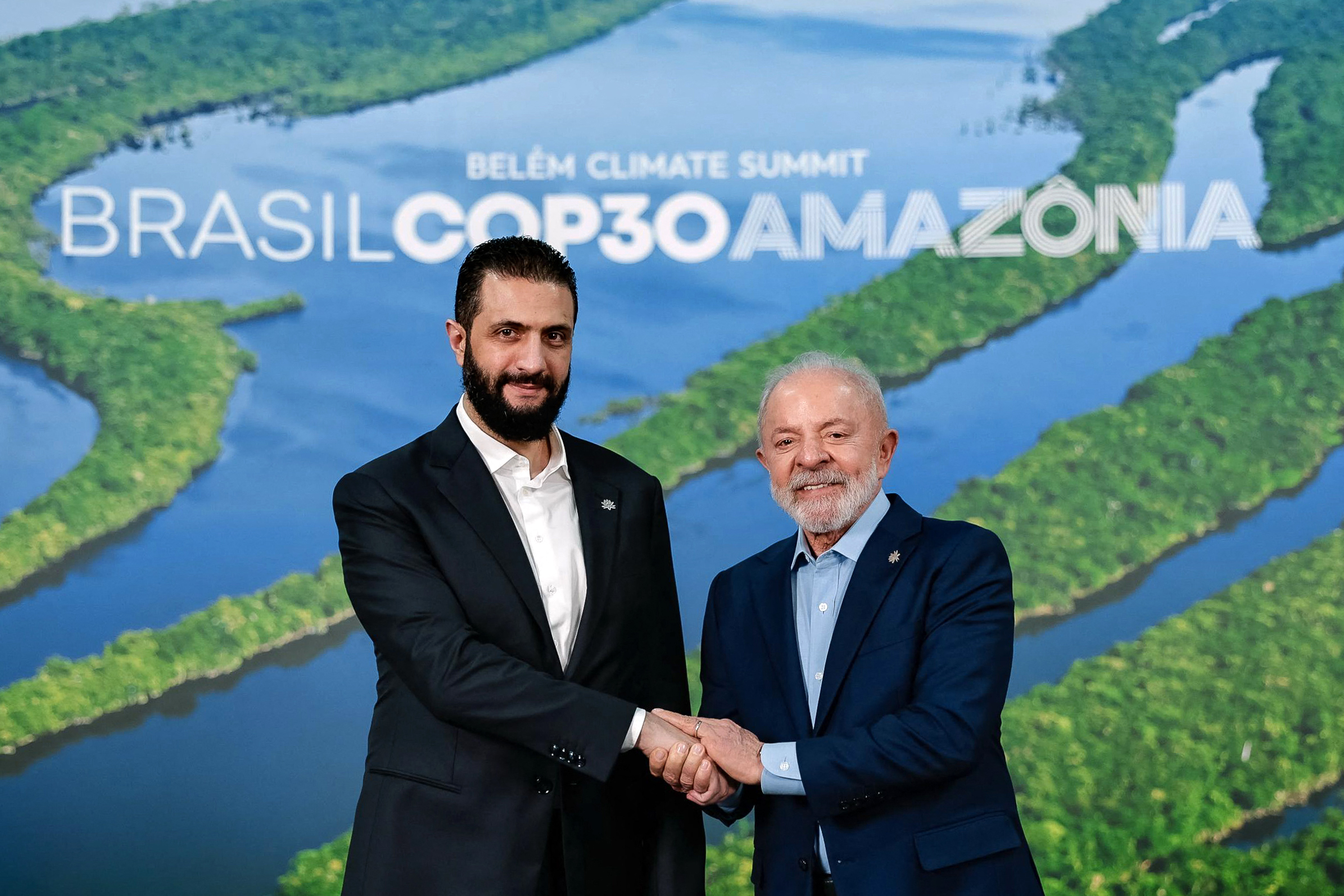 Brazil's President Luiz Inacio Lula da Silva (R) and Syria's President Ahmad Al Sharaa shake hands and pose for the camera.