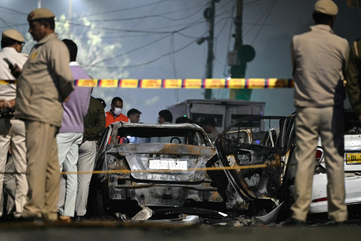Security personnel stand beside charred vehicles at the blast site.