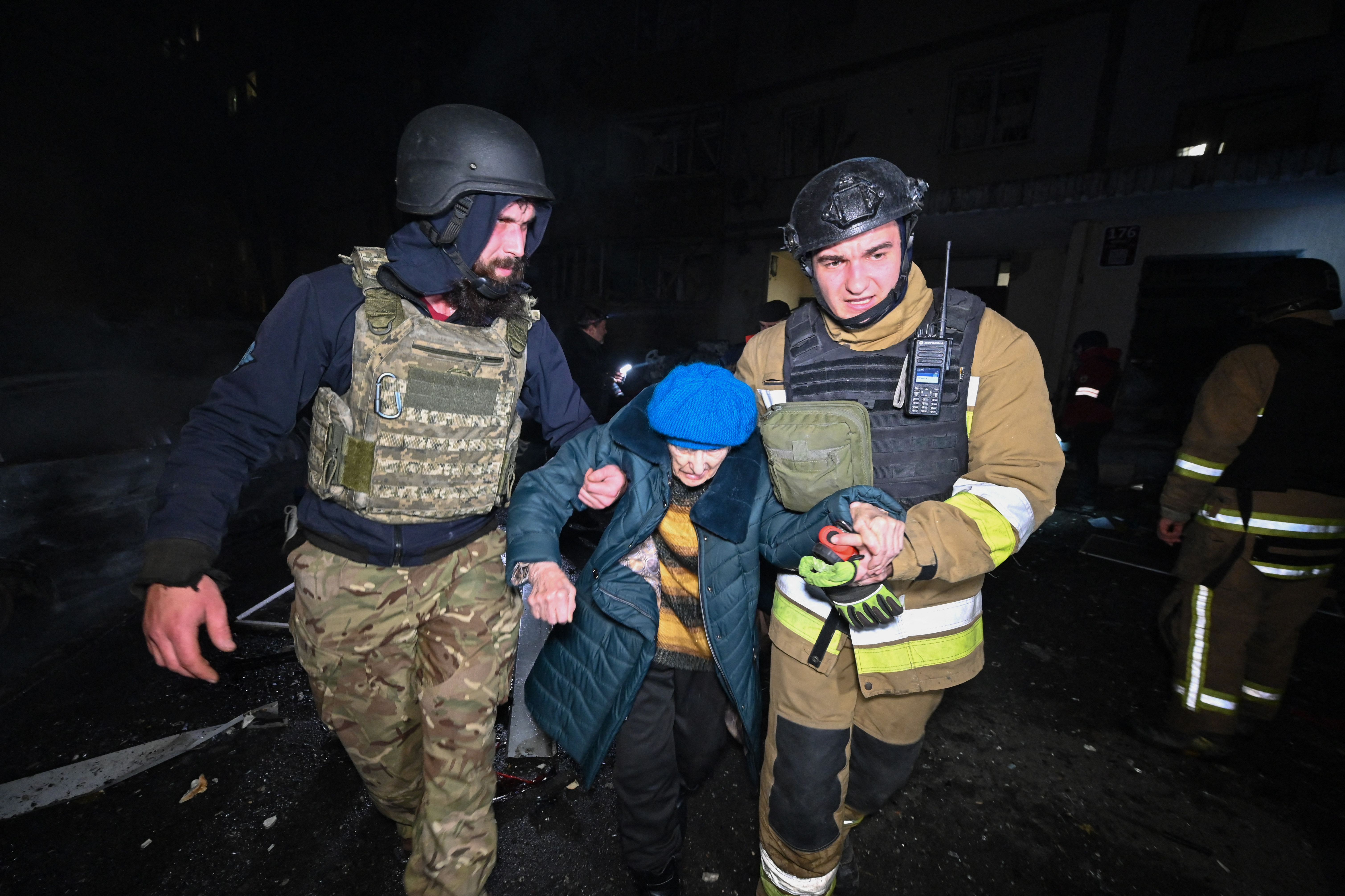 Ukrainian rescuers assist an elderly resident for her evacuation at the site of a Russian strike in Kharkiv, early on November 19, 2025, amid the Russian invasion of Ukraine. An overnight Russian drone strike wounded at least 36 people in Ukraine's Kharkiv, authorities said on November 19, 2025, the third such attack on the eastern region in three days. (Photo by SERGEY BOBOK / AFP)