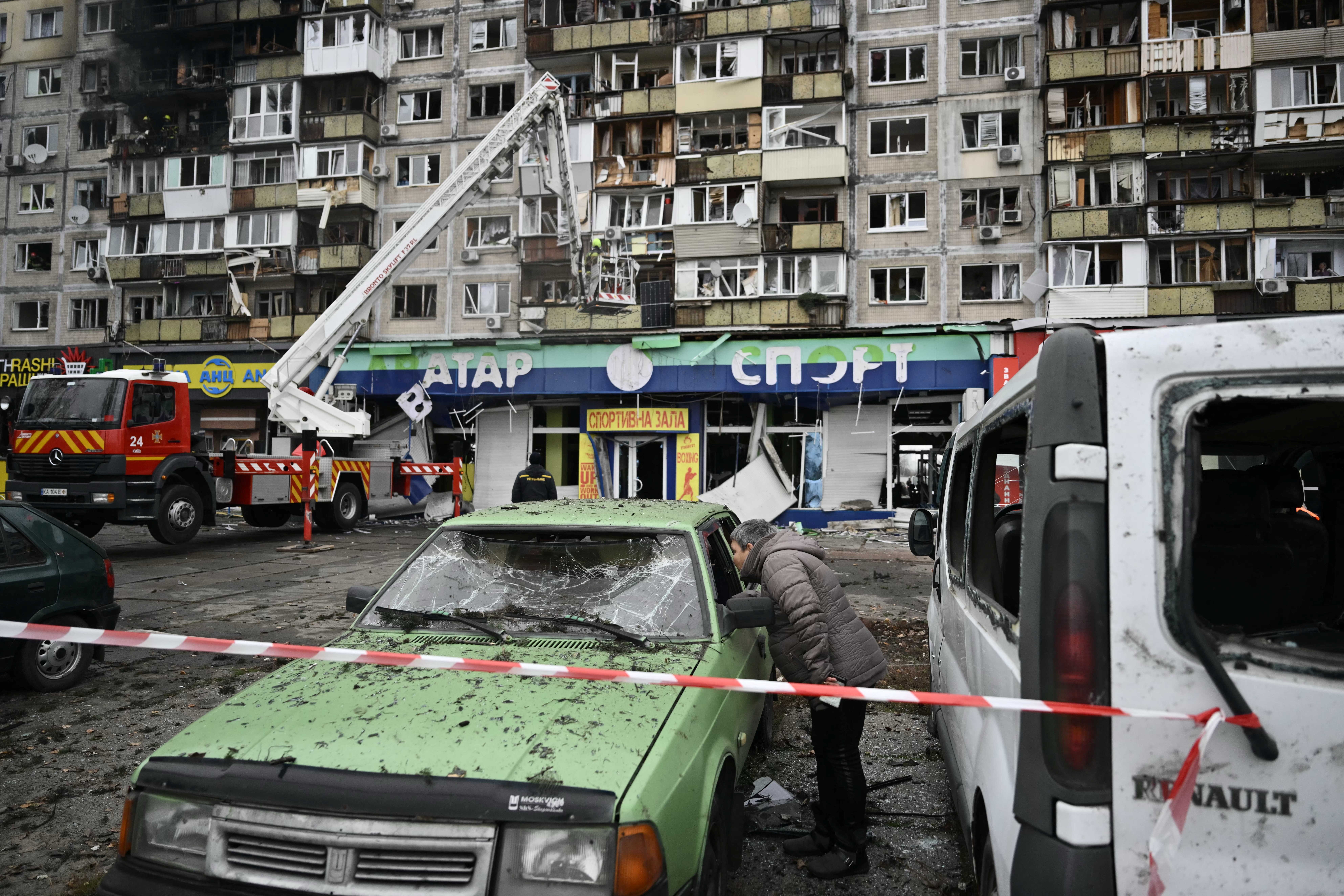 A local resident inspects a damaged car in front of a damaged residential building following an air attack in Kyiv