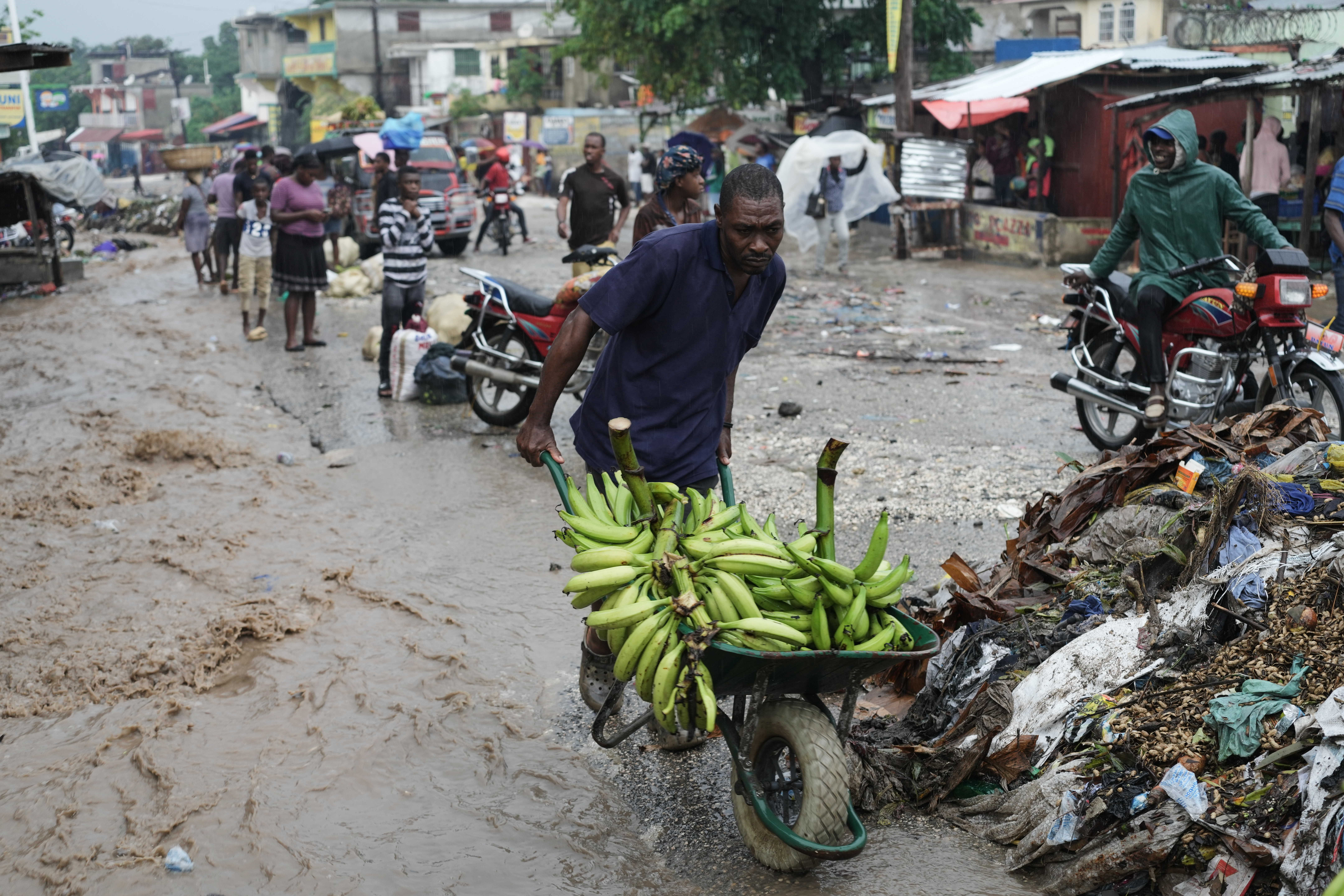 A man carts a wheelbarrow of bananas through a muddy street in Haiti