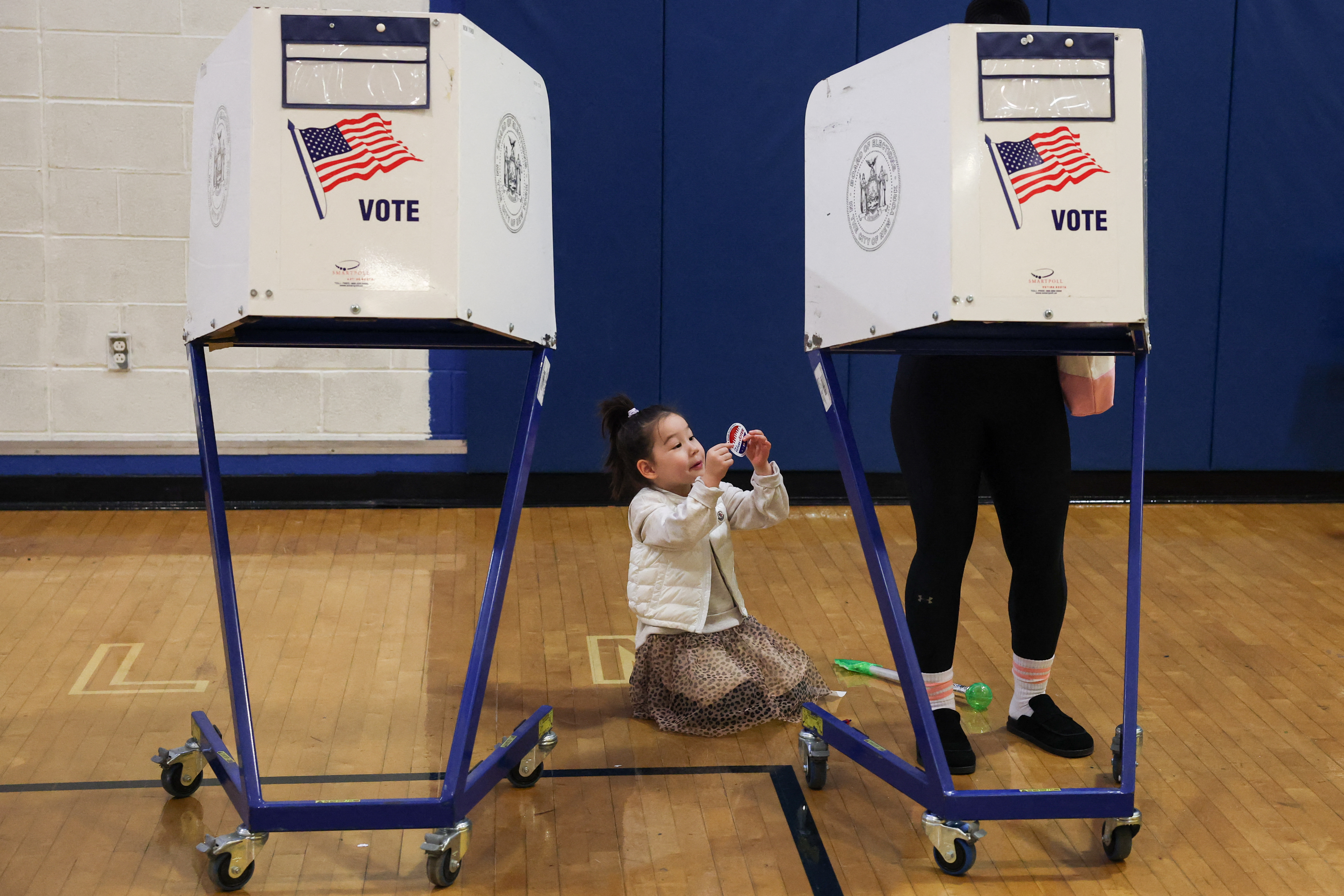 A child sits on the floor as an adult votes at a polling location at the High School of Art and Design in the Manhattan borough of New York City on November 4, 2025.