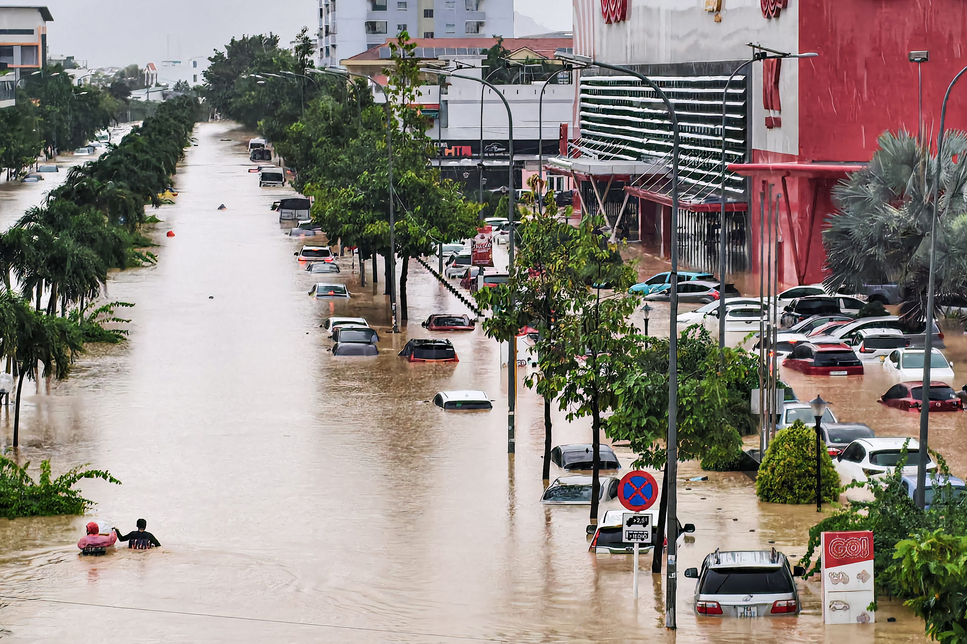 People (L) wade through floodwaters near inundated vehicles in Nha Trang, Vietnam's coastal province of Khanh Hoa on November 20, 2025.