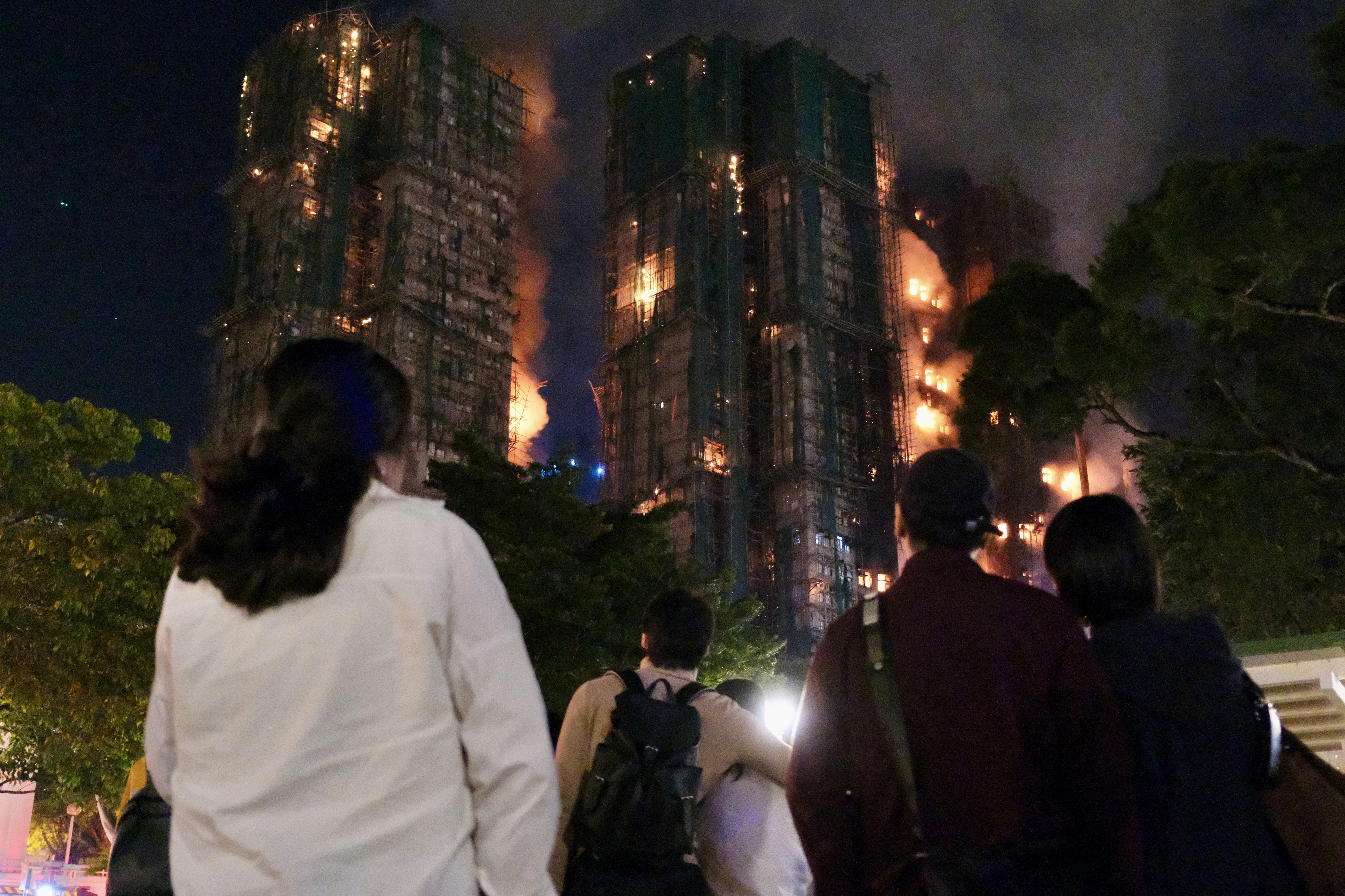 People look on as thick smoke and flames rise during a major fire at the Wang Fuk Court residential estate in Hong Kong's Tai Po district on November 26, 2025.