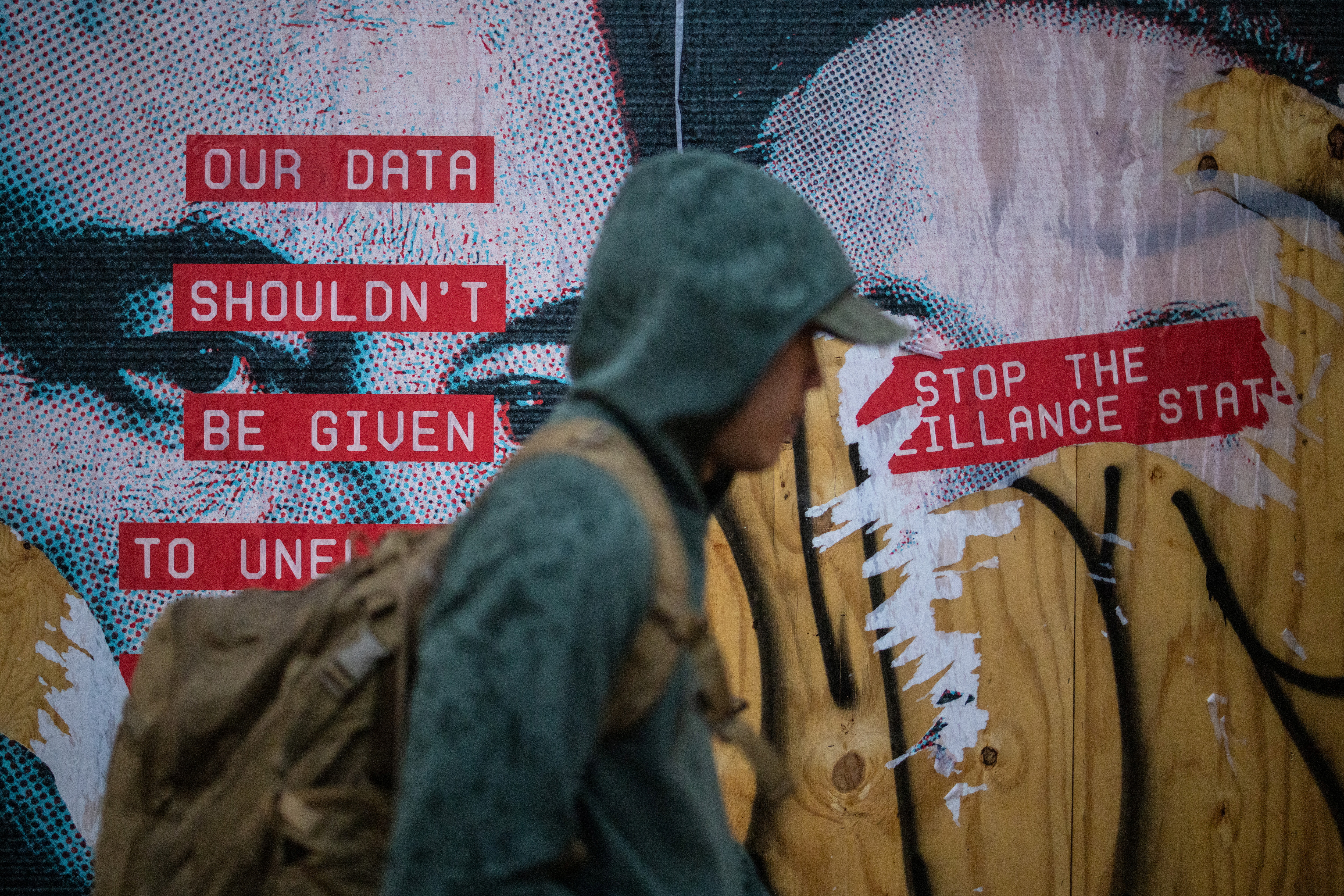 A person in a hoodie walks past a poster of Elon Musk
