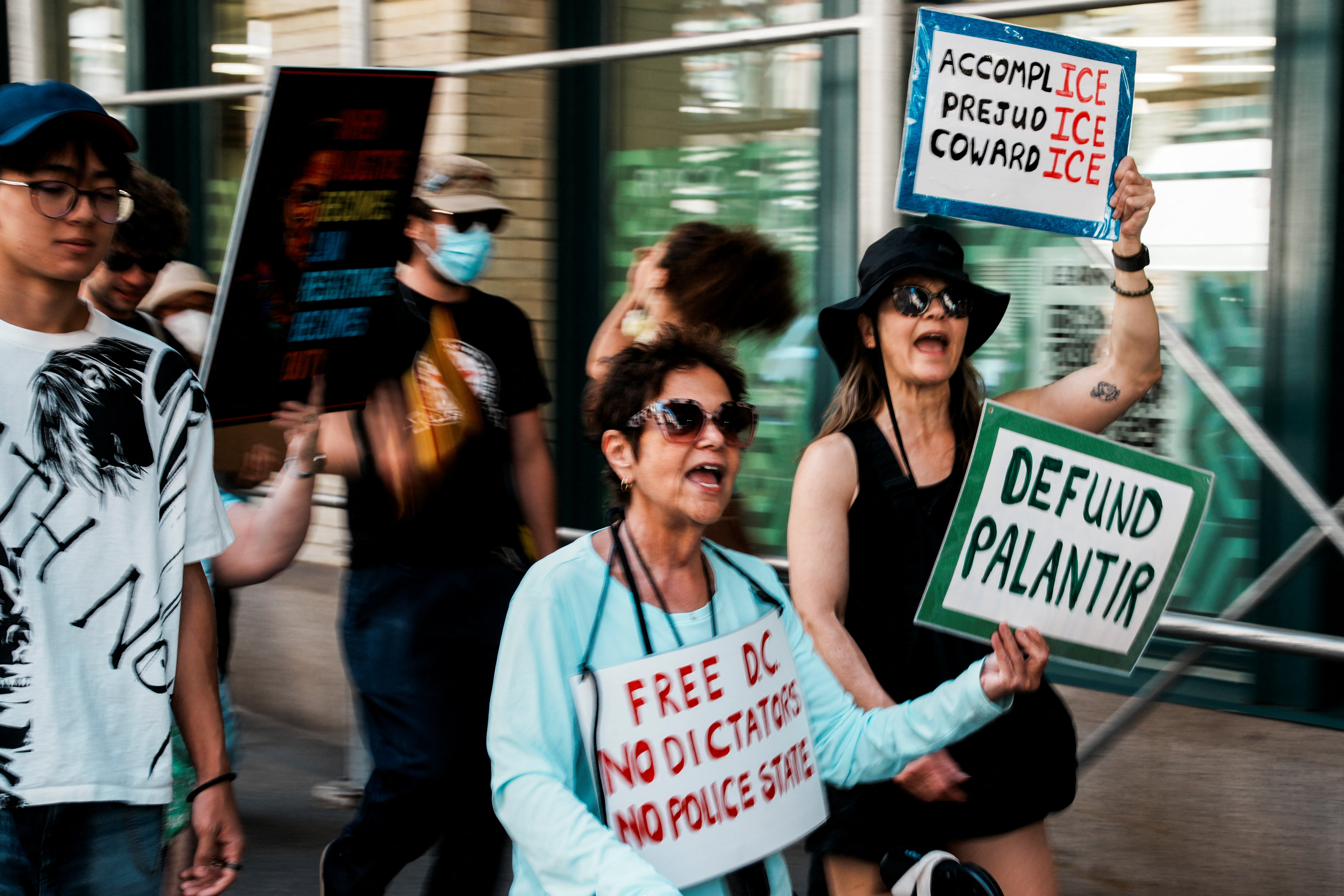 Protesters hold up signs to "defund Palantir" and "free DC"