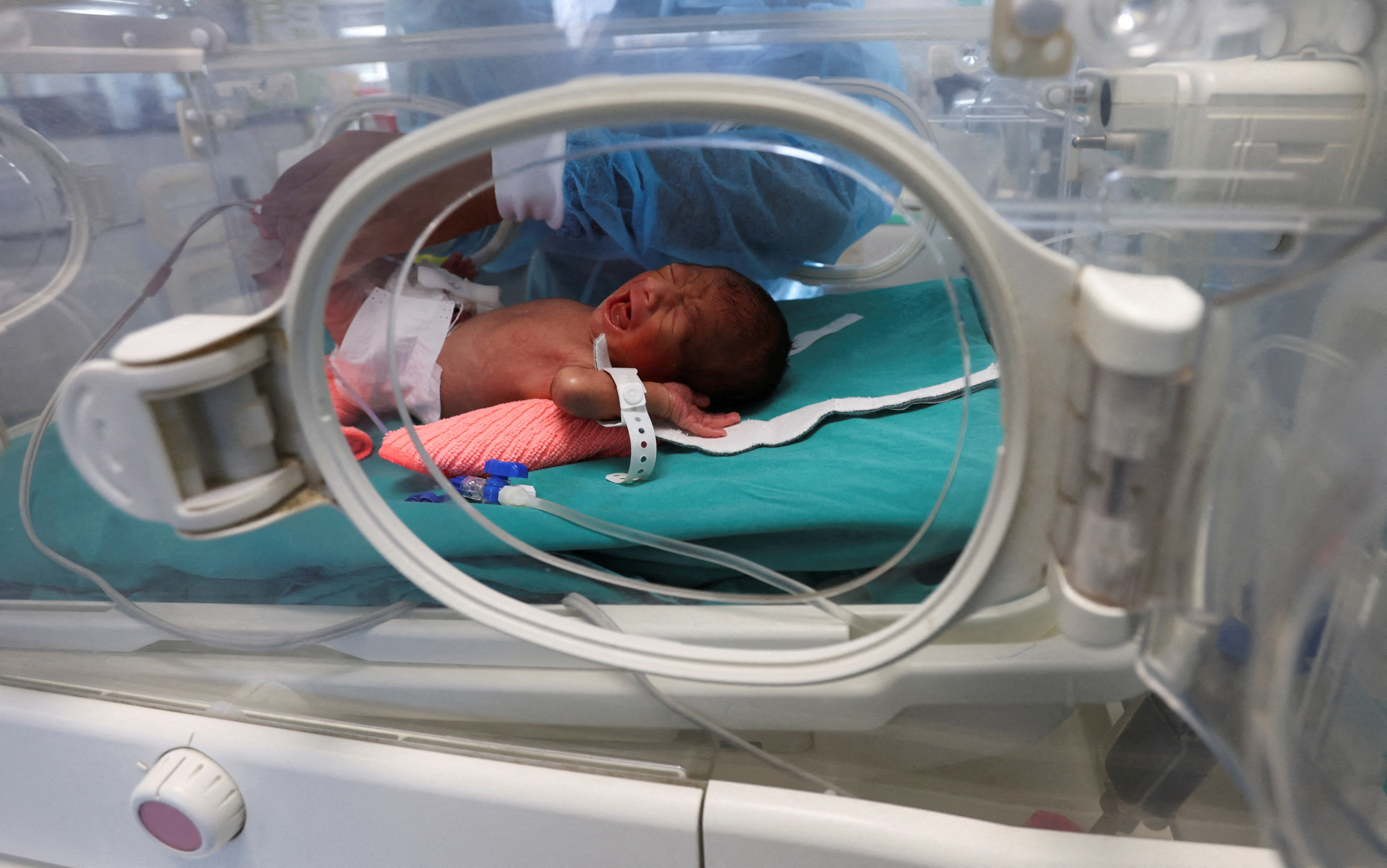 A medical worker examines a baby inside an incubator at a hospital.