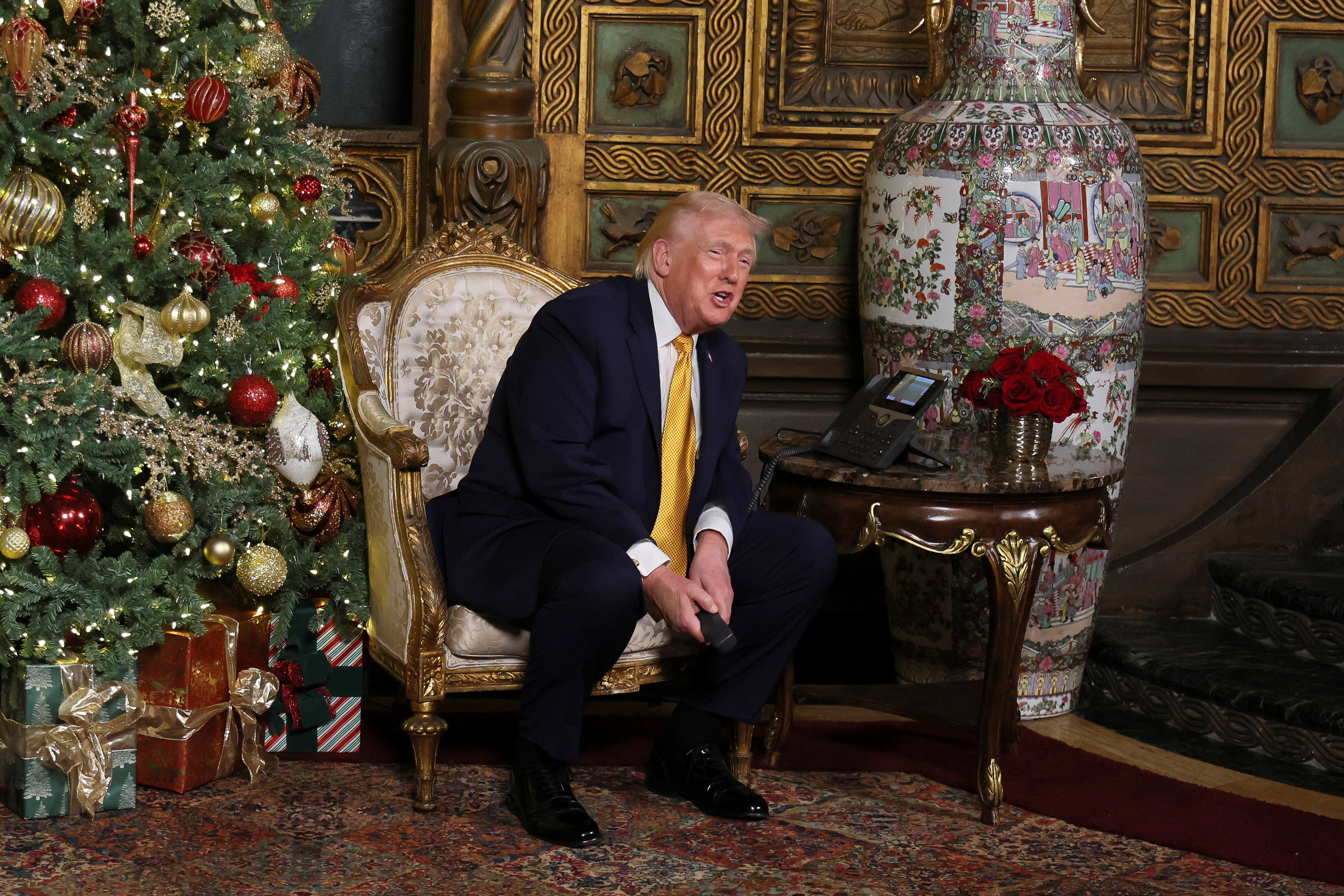 Trump uses a speakerphone to respond to children as he sits next to a Christmas tree