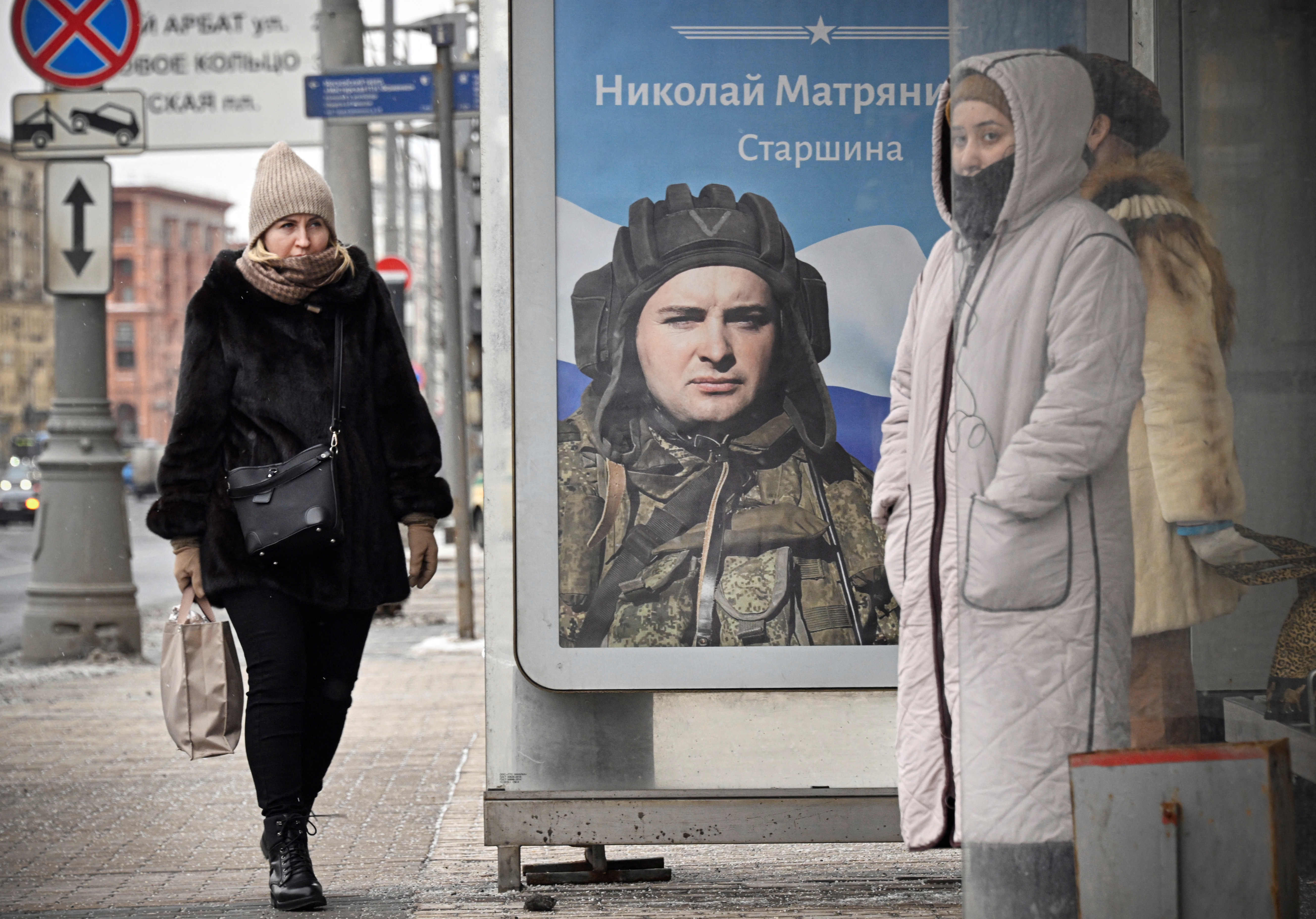 People wait at a bus stop next to a poster displaying Russian Army Master Sergeant Nikolai Matryanitsky, participating in Russia's military action in Ukraine, in central Moscow on February 15, 2023. (Photo by Alexander NEMENOV / AFP)