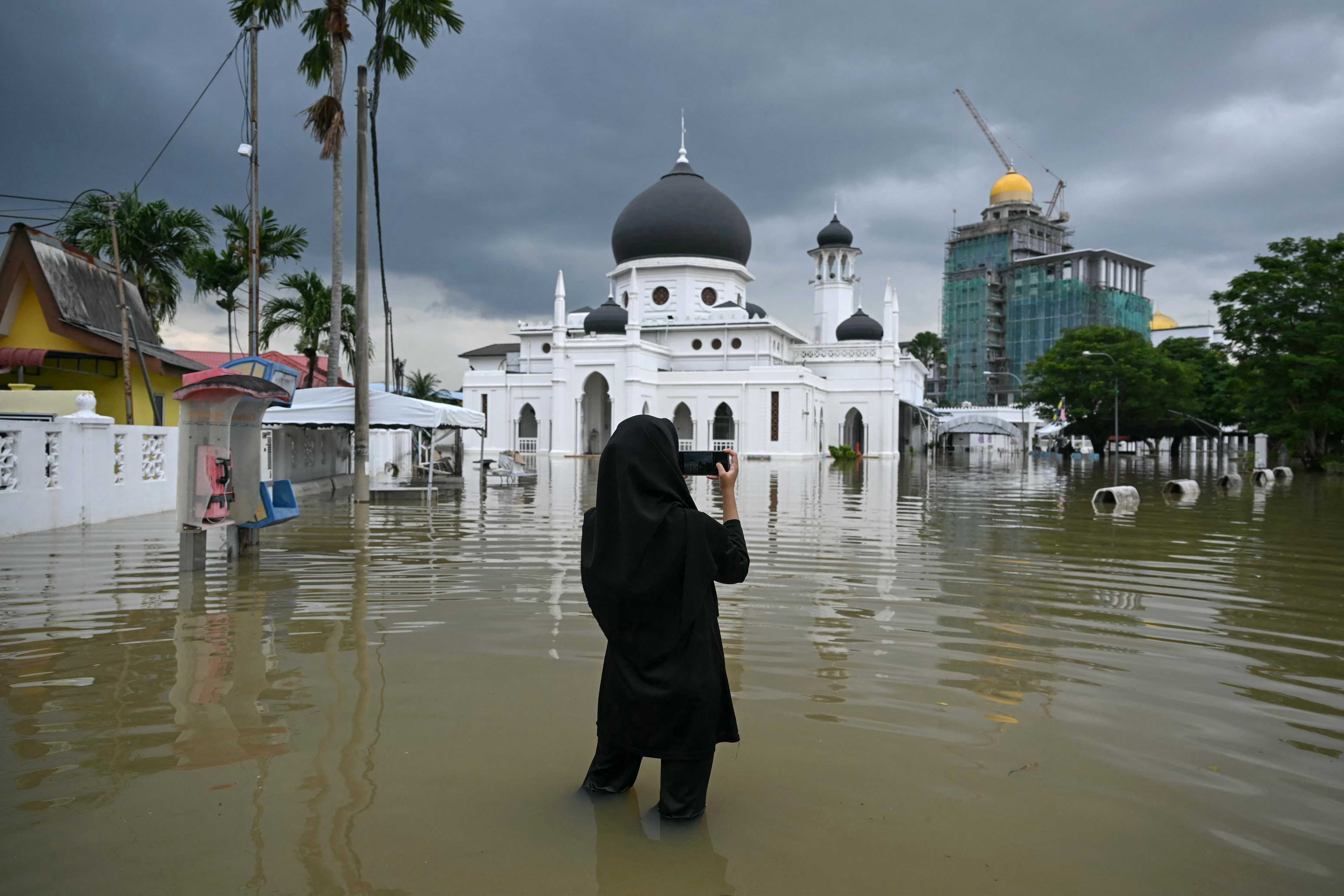 A woman takes a photo of a flooded mosque in Kangar in northern Malaysia's Perlis state on November 27, 2025, as severe flooding affected thousands of people in the region following days of heavy rain. Flooding in Malaysia from days of heavy rain has swept through eight states, with forecasters predicting more rain in the coming days. More than 27,000 people were evacuated to dozens of temporary shelters this week, with one death recorded in one of the worst-hit states, Kelantan, on the northeastern coast, according to rescue officials. (Photo by MOHD RASFAN / AFP)