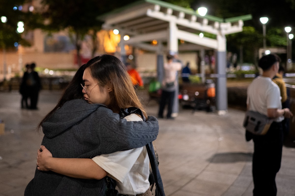 People hug at a makeshift memorial outside the Wang Fuk Court apartment blocks in the aftermath of the deadly November 26 fire in Hong Kong's Tai Po district on December 1, 2025.Hong Kong has arrested 14 suspects in a probe into the city's deadliest fire in decades, finding "substandard" netting on building exteriors that failed to halt flames from spreading, authorities said on December 1, 2025.