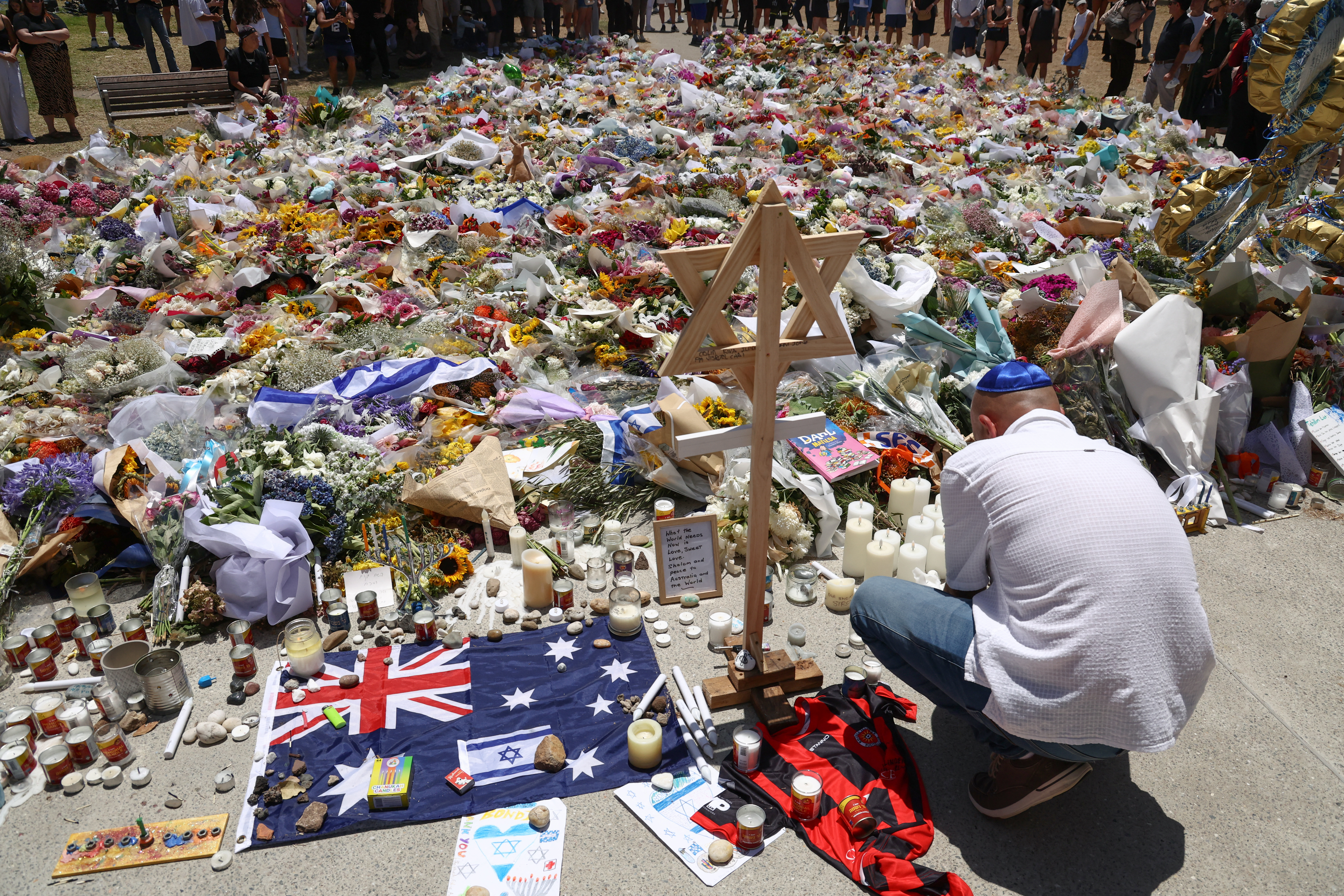 A mourner lights candles as people gather around floral tributes outside Bondi Pavilion in Sydney on December 17, 2025, to honour victims of the Bondi Beach shooting. Australia held the first funeral on December 17 for victims of the Bondi Beach mass shooting, as large crowds gathered to grieve a rabbi slain in the attack. Sajid Akram and his son Naveed opened fire on a Jewish festival at the famed surf beach on December 14 evening, killing 15 people and wounding dozens more. (Photo by DAVID GRAY / AFP)