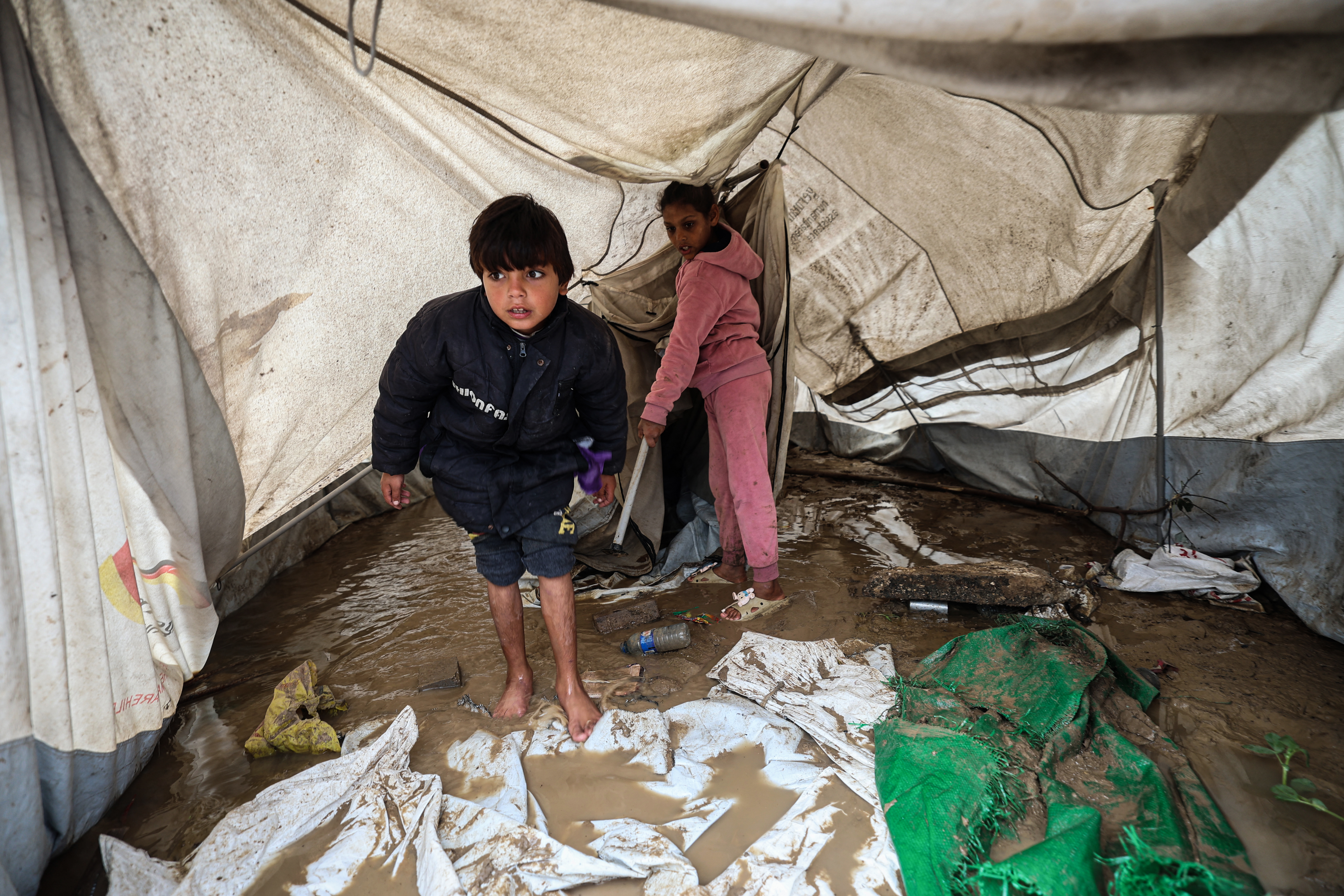 Young displaced Palestinians stand inside a tent flooded with rainwater in the Bureij refugee camp
