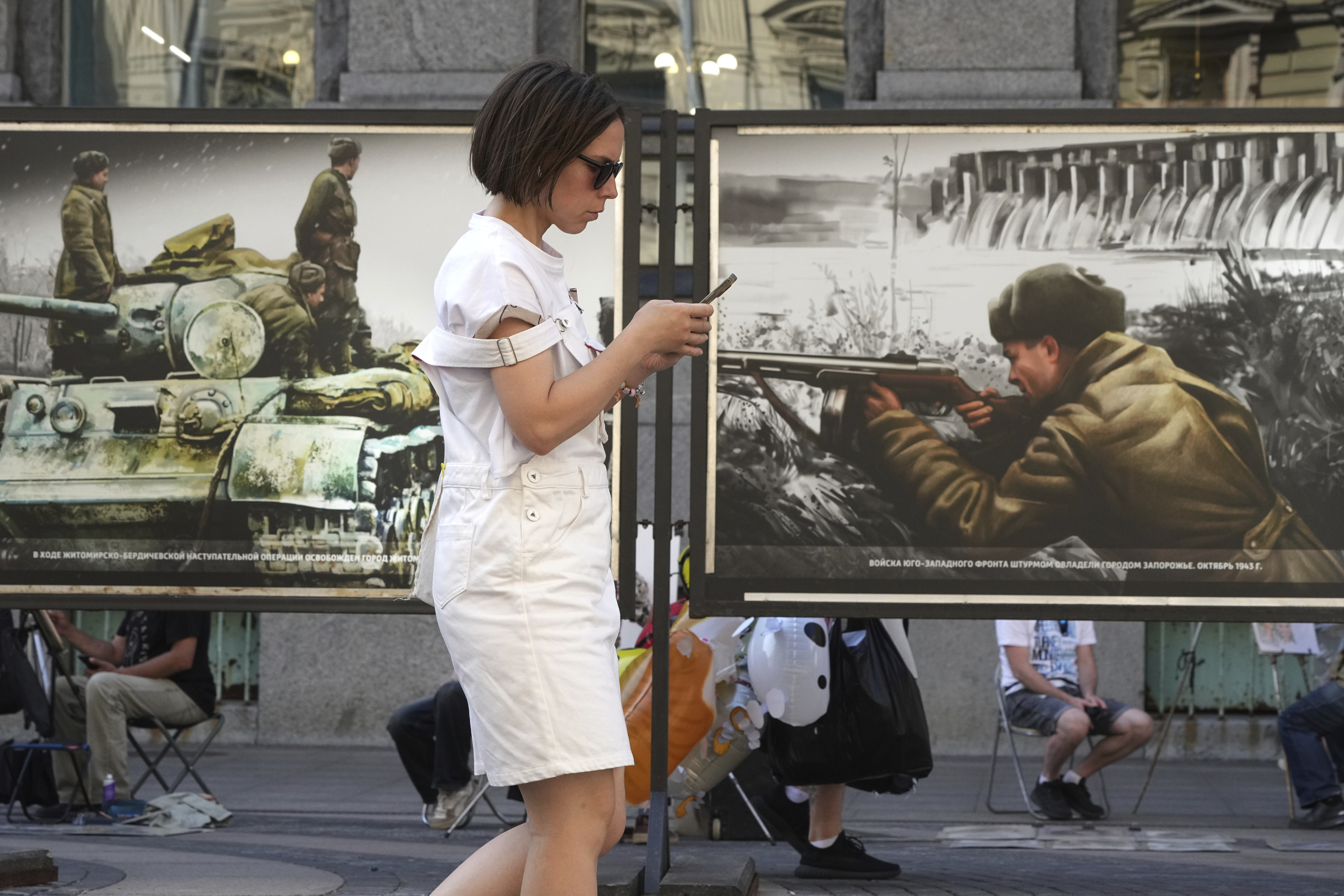 A woman looks at her phone while passing a street exhibition of World War II-era colorized photos in St. Petersburg, Russia, on Monday, July 14, 2025. (AP Photo/Dmitri Lovetsky)