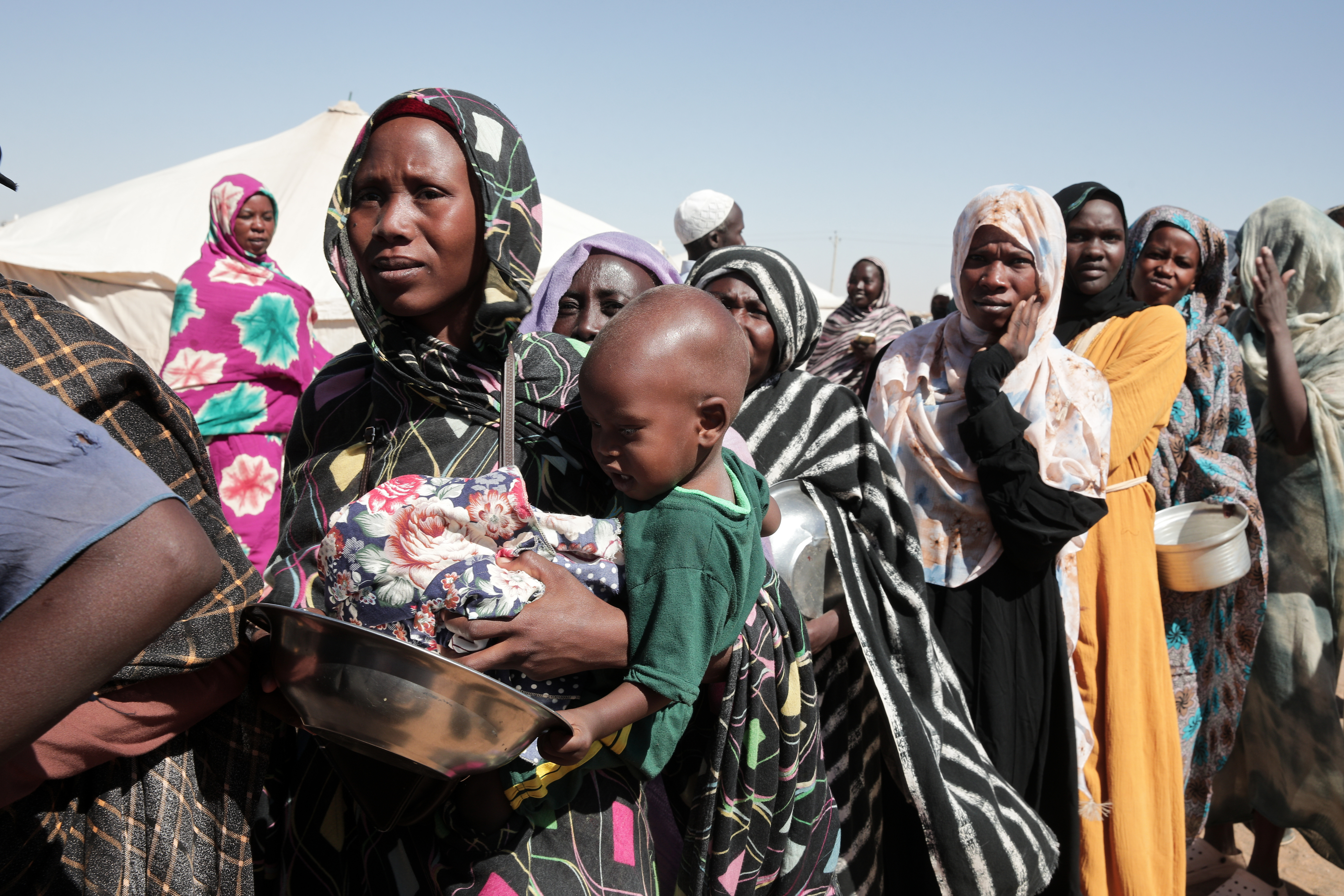 Displaced women carrying young children stand in line to receive food aid.