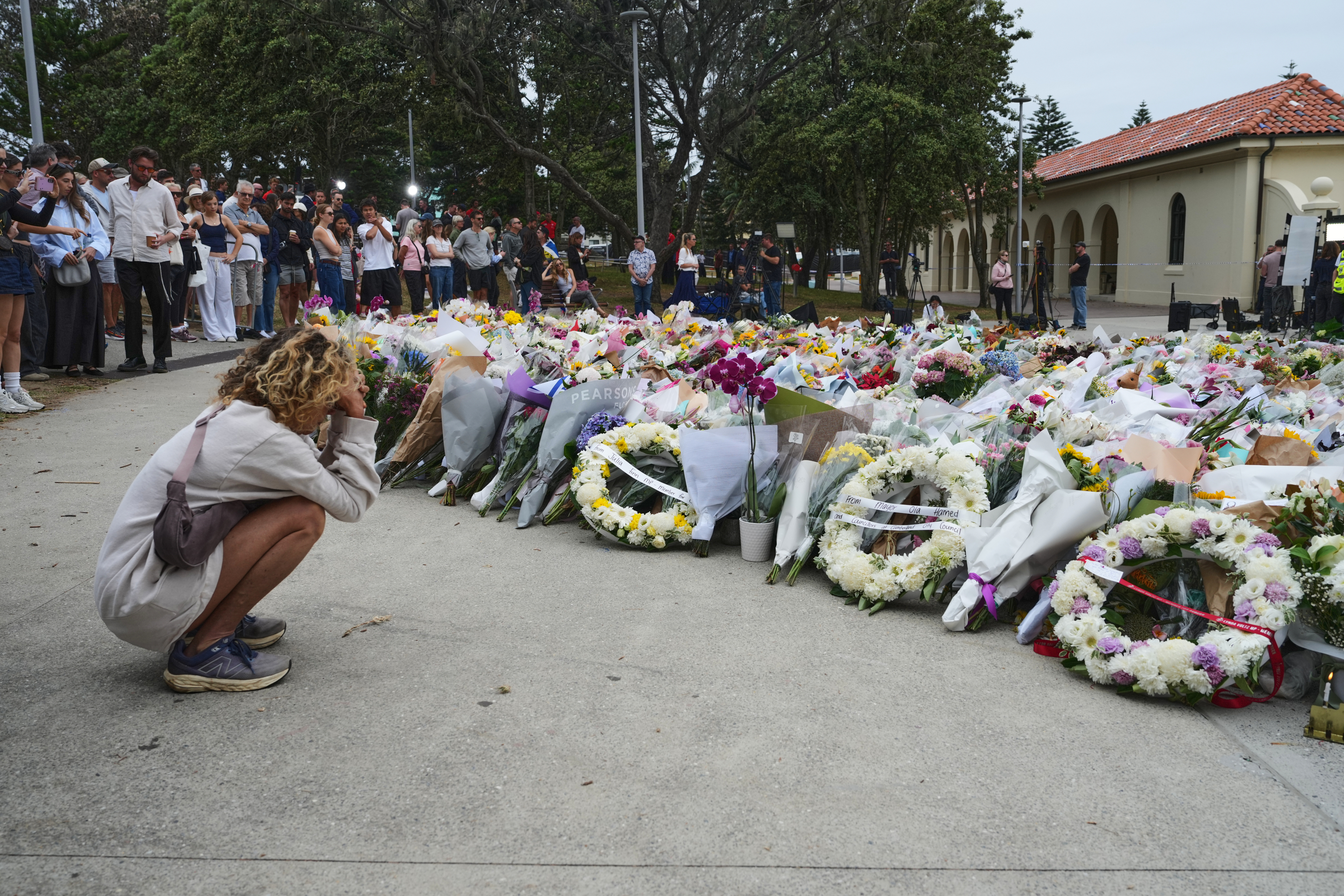 A young woman kneels down by a floral tribute by the Bondi Pavilion in Sydney, Australia